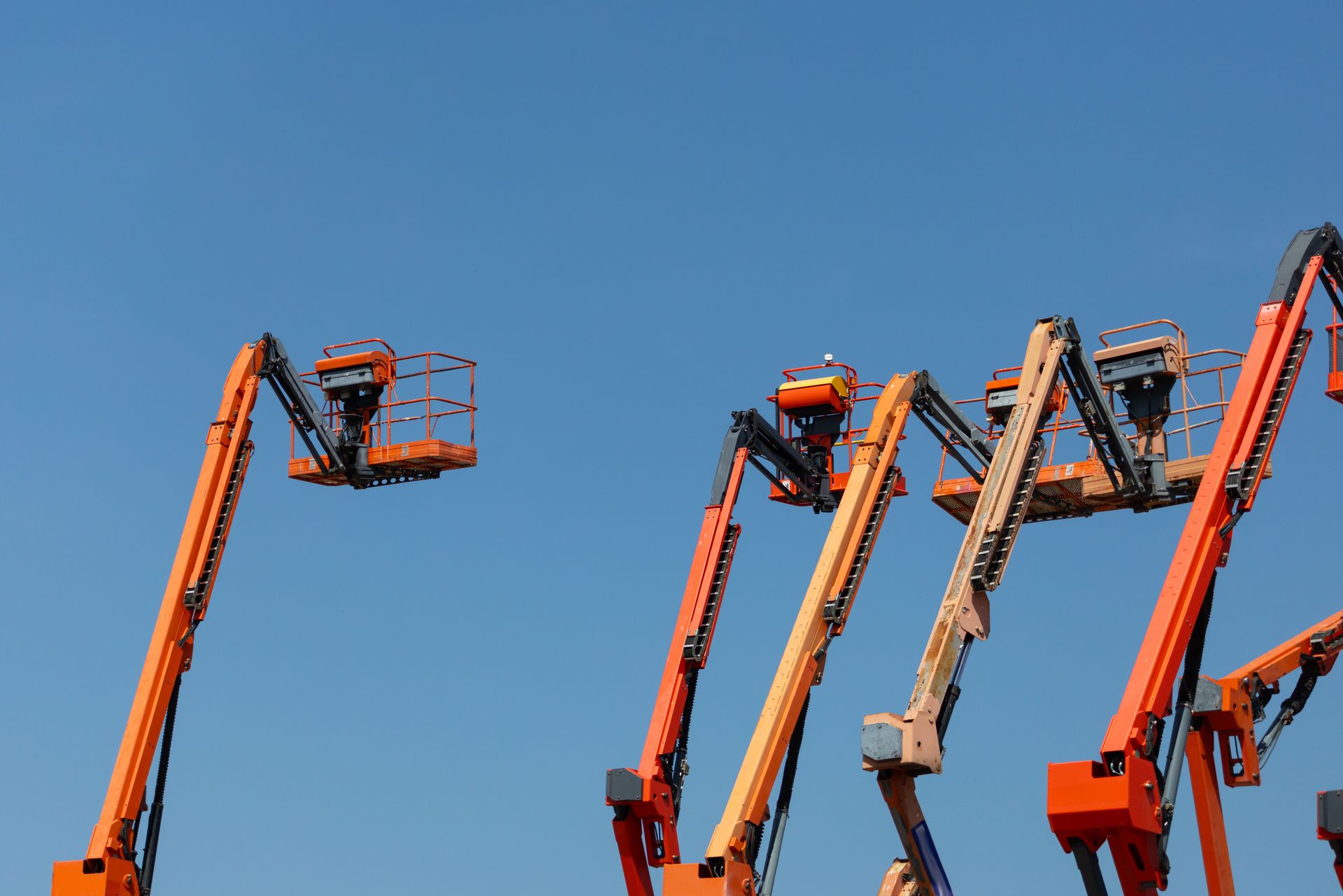 Multiple aerial lift boom cranes extended upward against a clear blue sky.