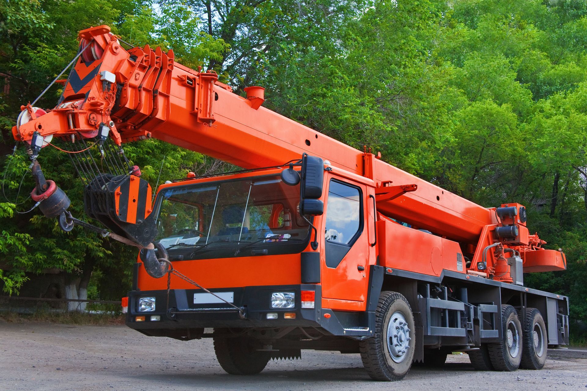 Orange mobile crane truck parked on a road beside green trees