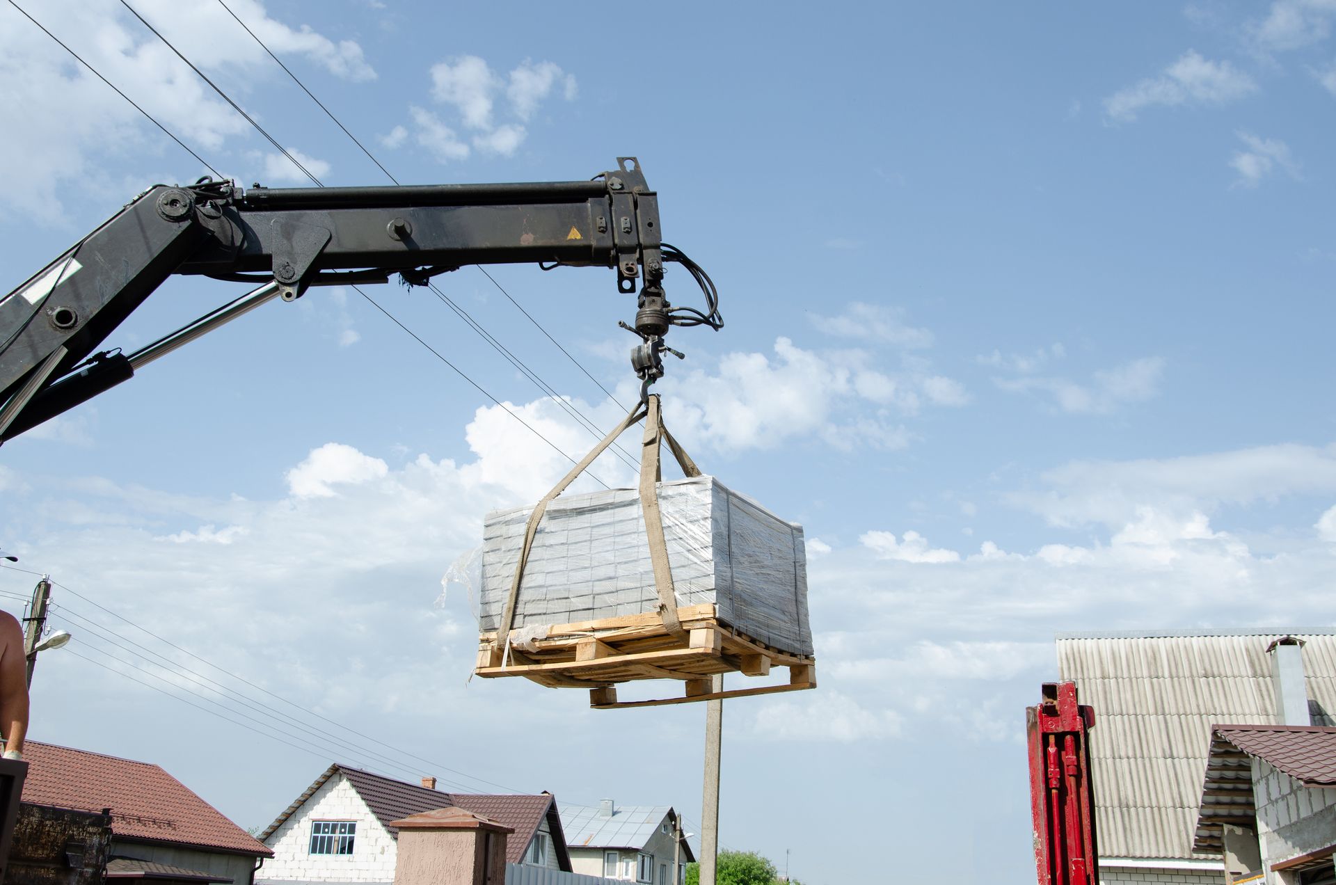 Crane lifting a wrapped pallet of materials against a blue sky at a construction site Crane lifting a wrapped pallet of materials against a blue sky at a construction site