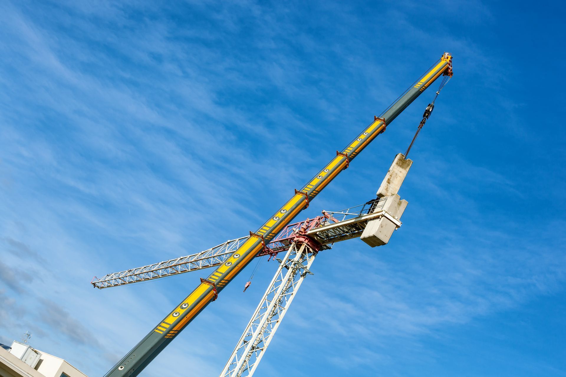Two cranes against a blue sky, one yellow and one white, lifting at a construction site