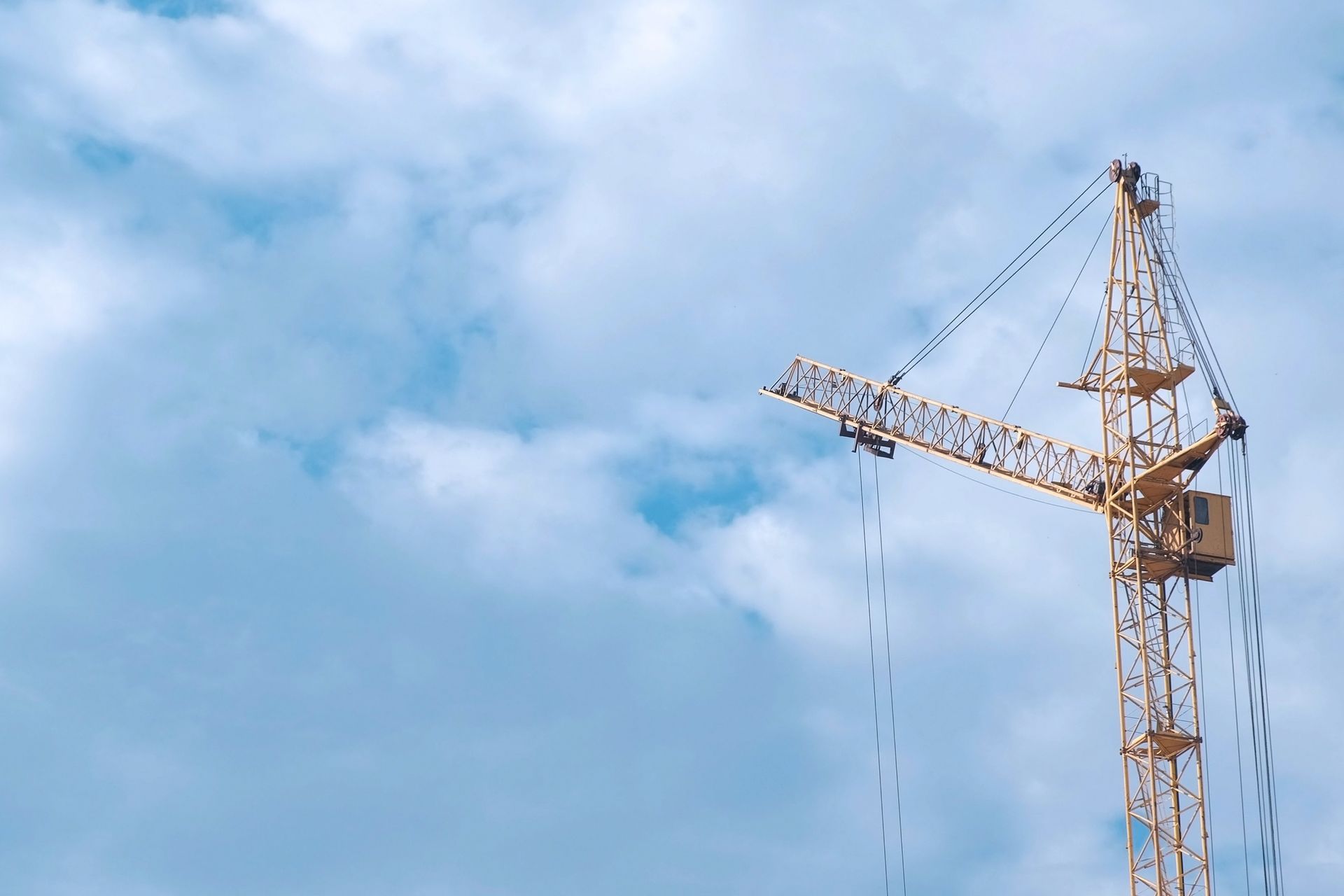 Tower crane against a cloudy blue sky, with hanging cables and a horizontal boom