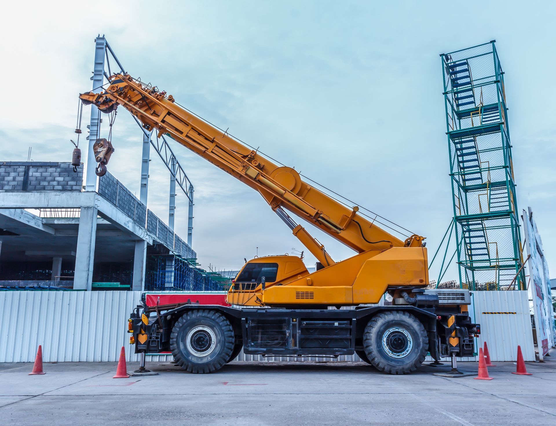 Orange mobile crane at a construction site, lifting a load beside a building frame and scaffolding