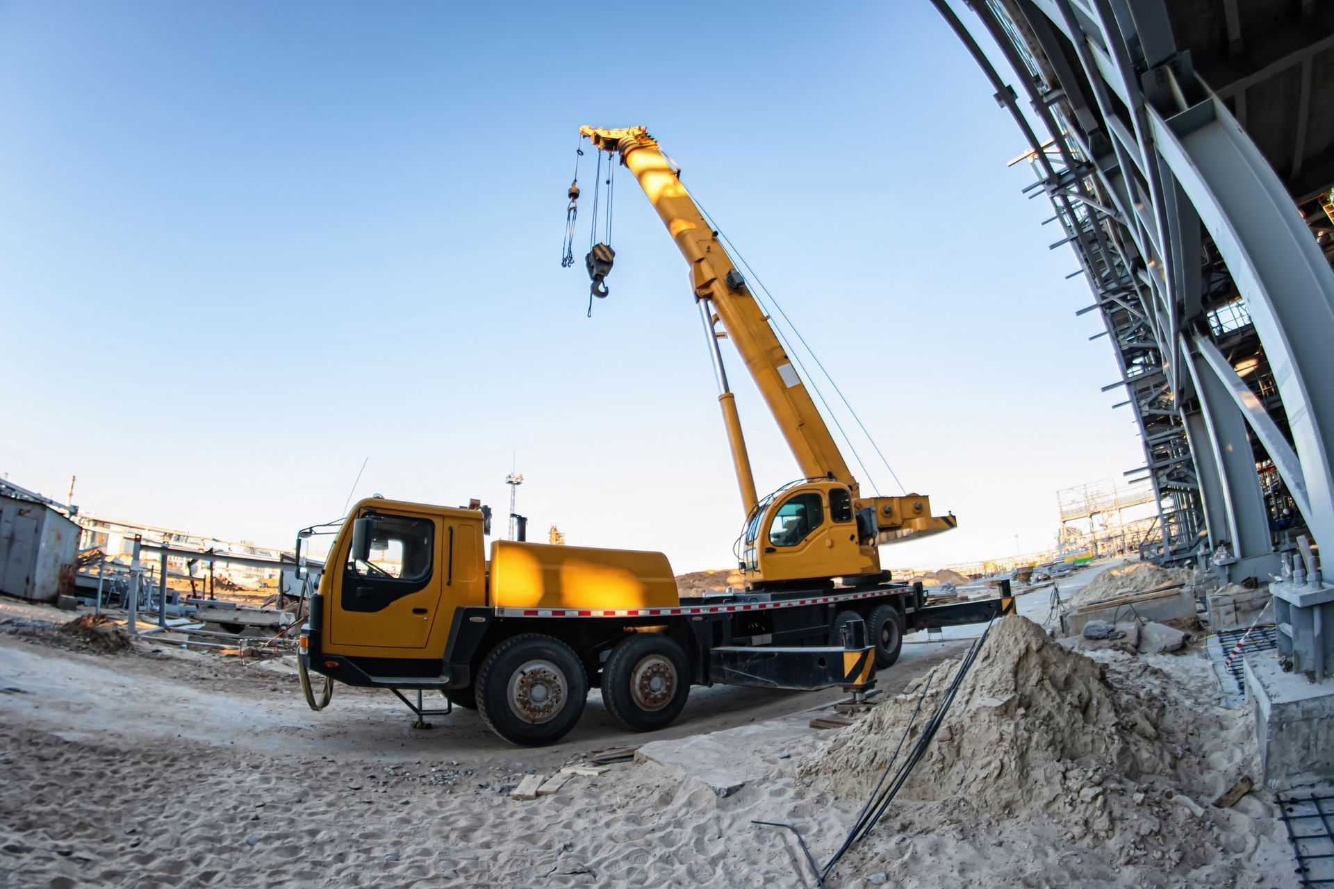 Yellow crane truck at a construction site lifting materials beside a steel structure in snowy conditions