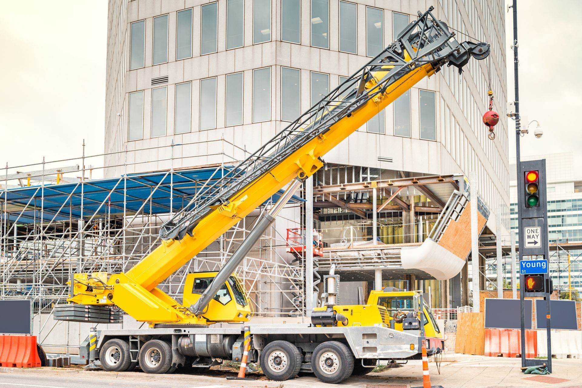 Yellow crane truck lifting a white bucket at a construction site beside a modern building