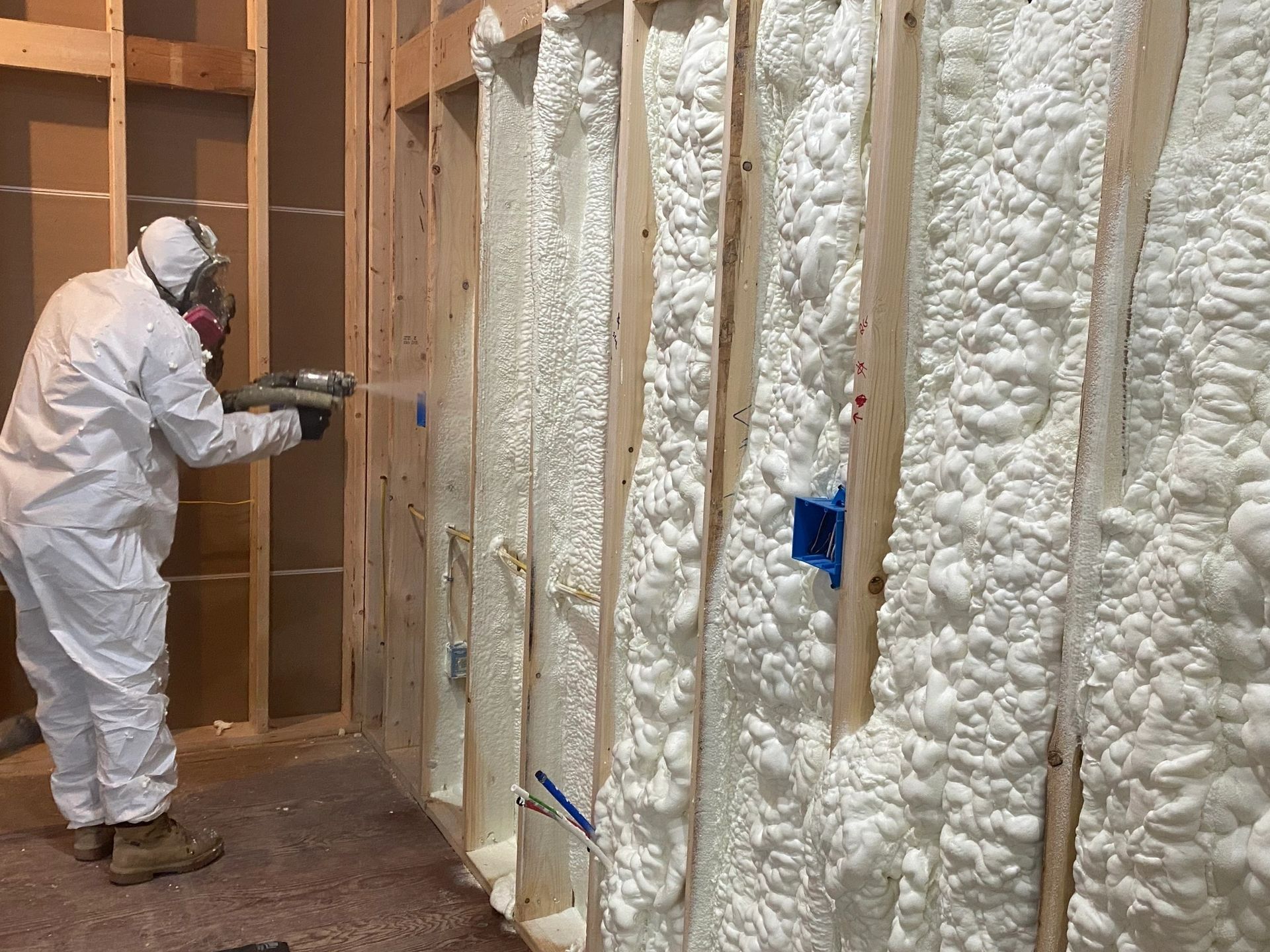 A man in a protective suit is spraying foam on a wall.