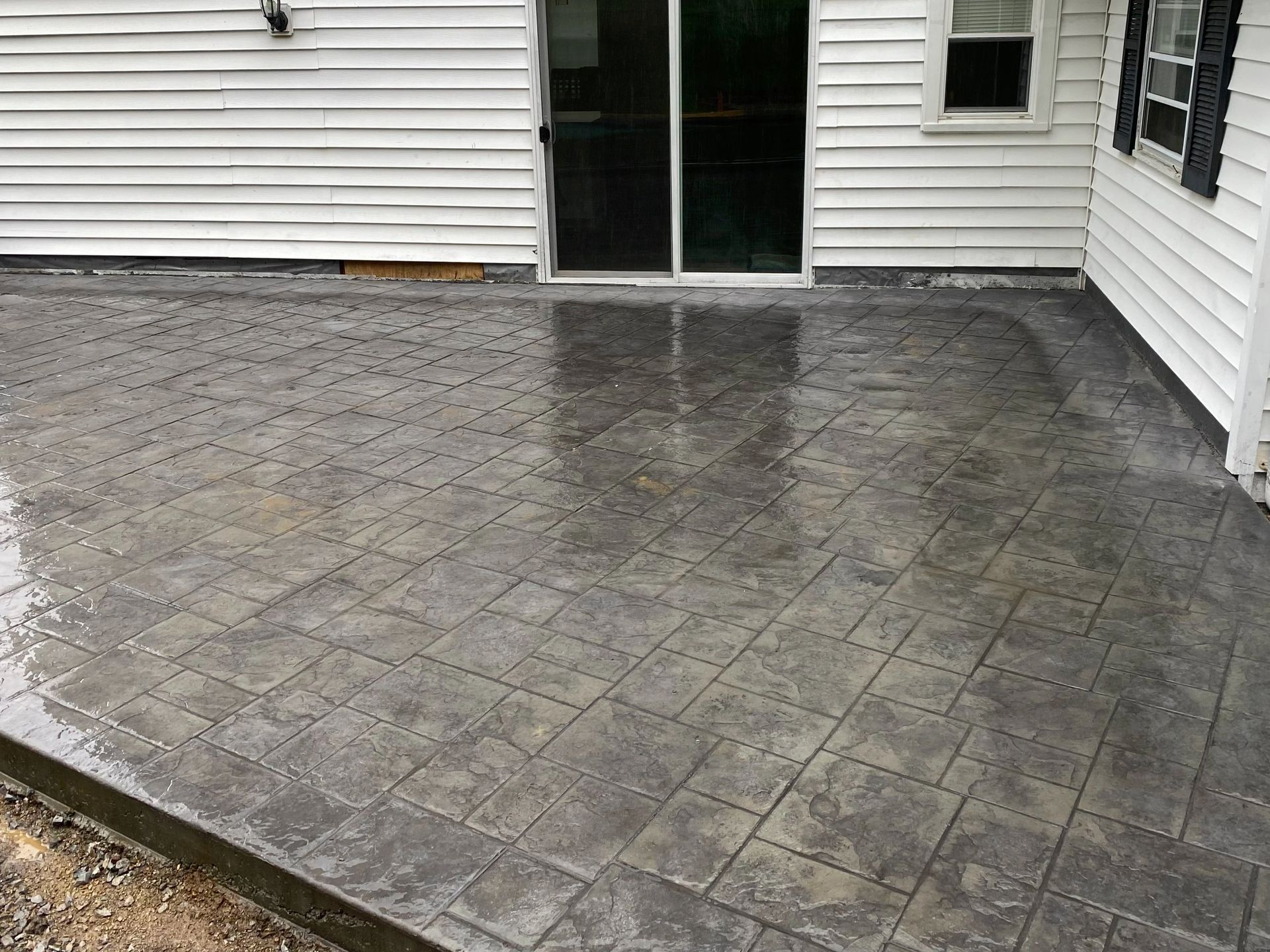 A concrete patio in front of a white house with a sliding glass door.