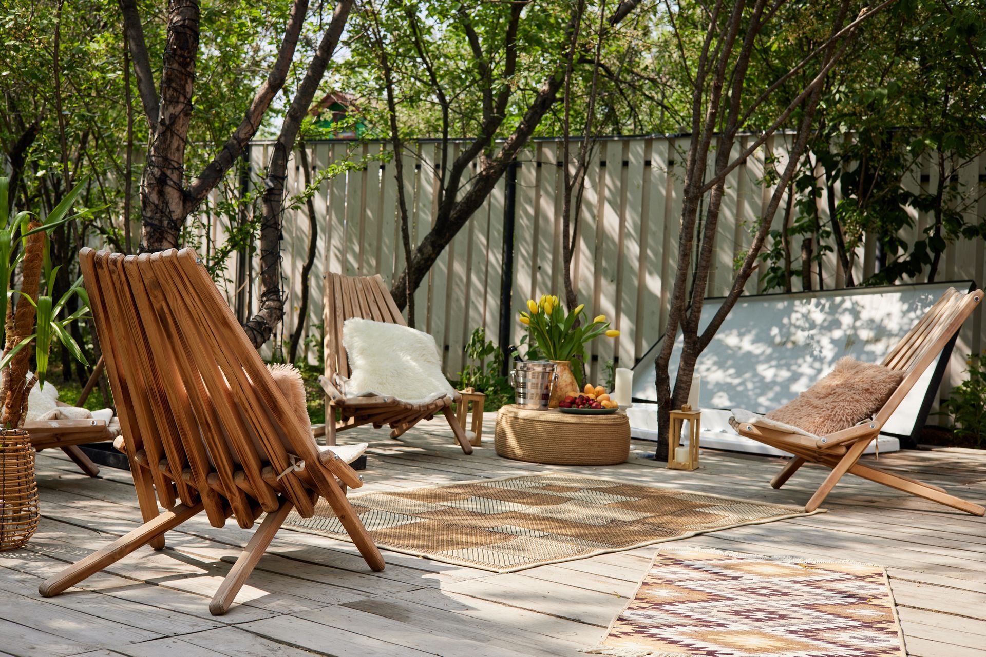Wooden chairs on a patio surrounded by trees and a neutral-toned rug.