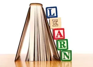 An open book stands upright with colorful alphabet blocks stacked beside it to spell the word