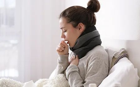 a woman is laying in bed with a scarf around her neck and coughing .