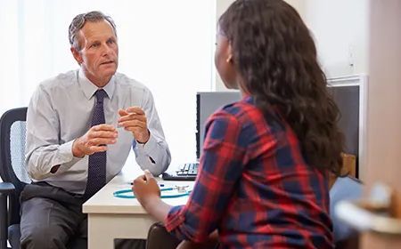 a doctor is sitting at a desk talking to a patient .