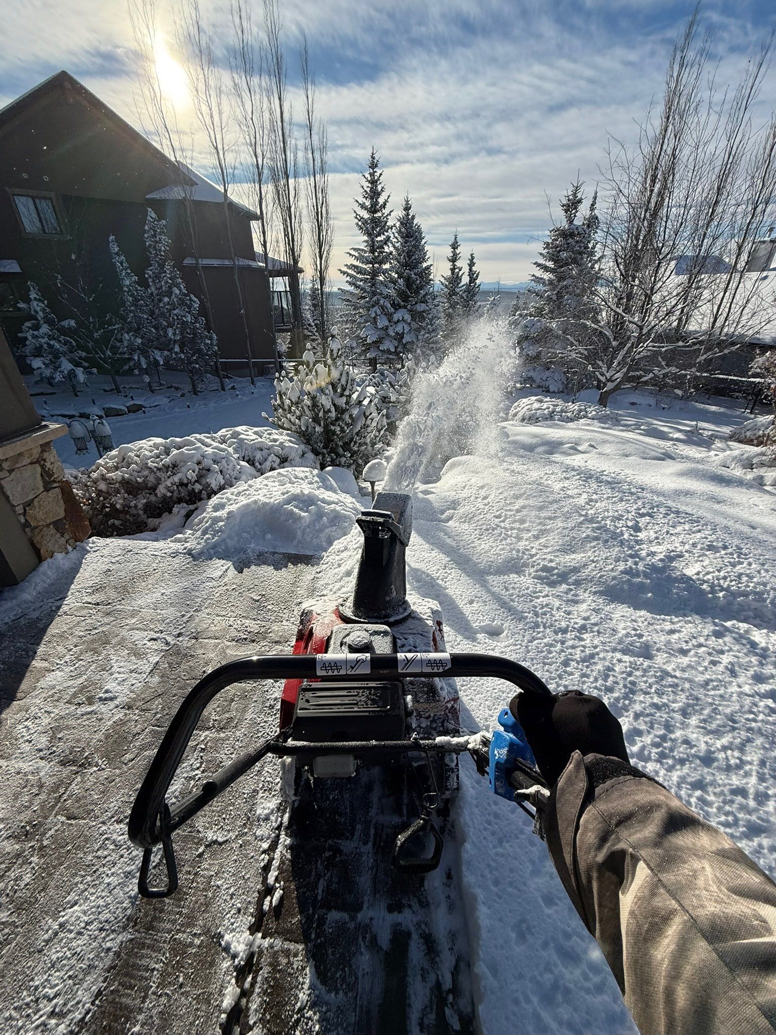 Snowblower clearing a snowy driveway on a sunny day.