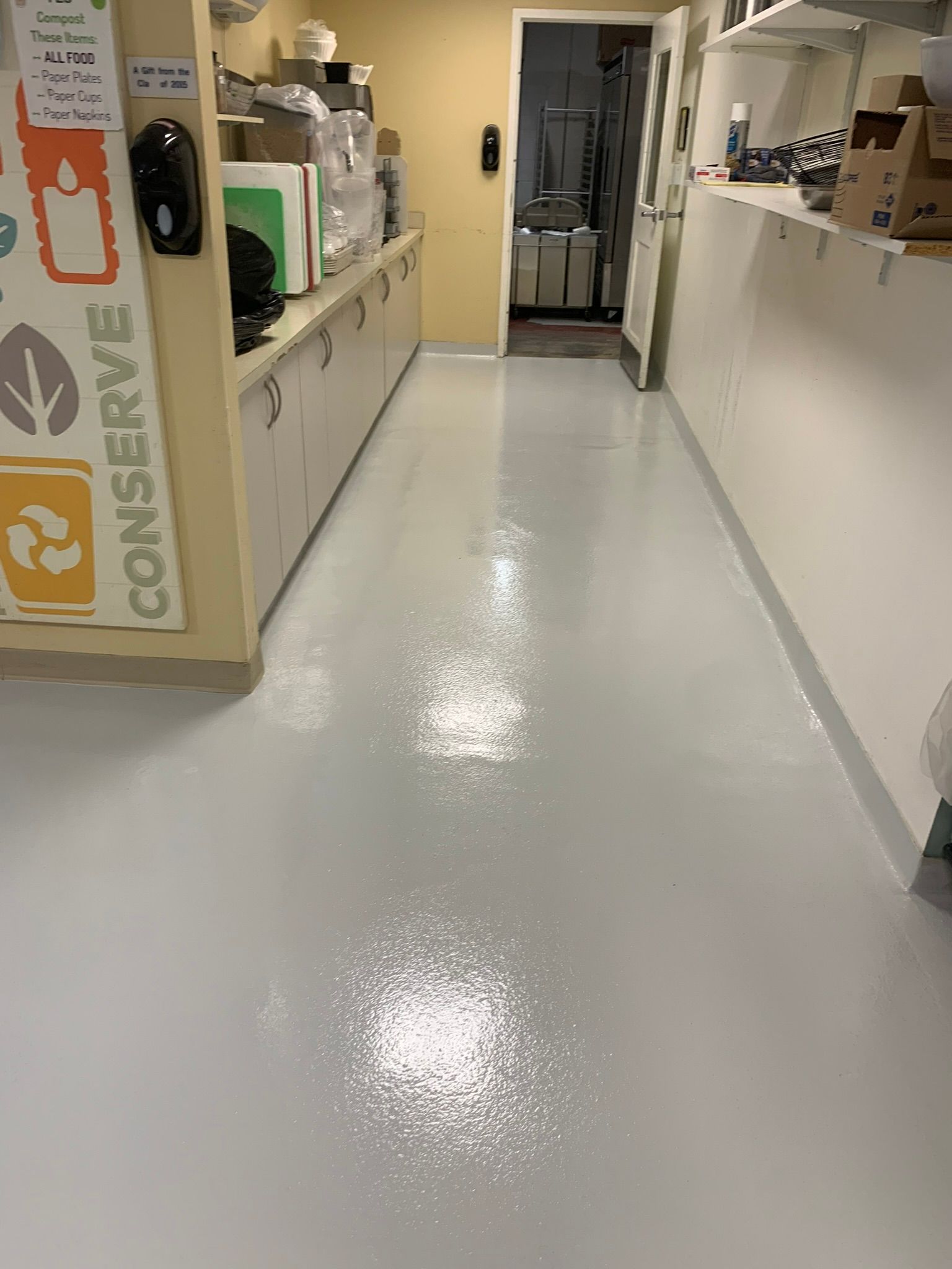 Shiny hospital corridor with white counters and a doorway at the end, viewed from the hallway.