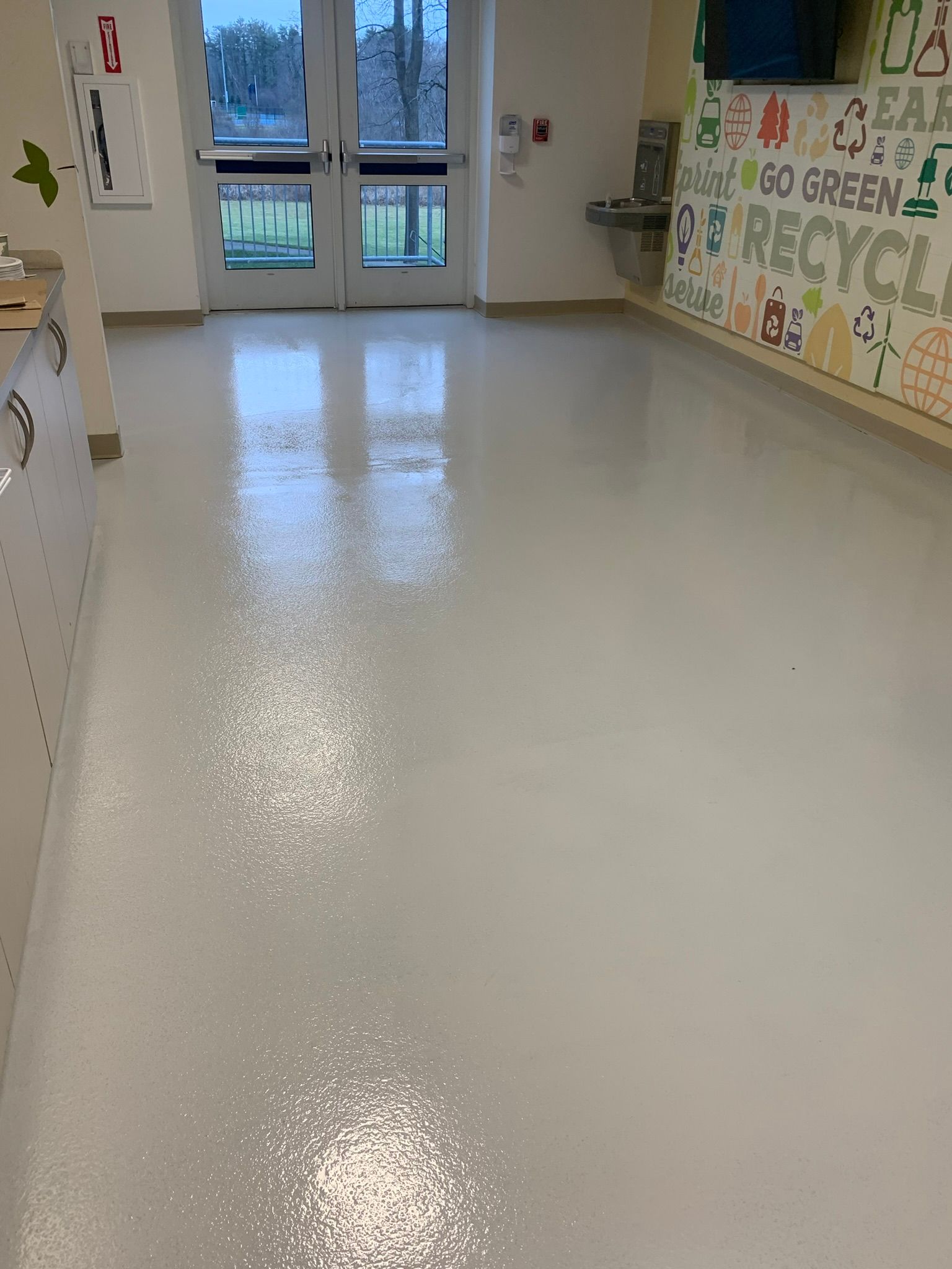 Empty school hallway with glossy white floor, colorful wall art, and glass doors at the end