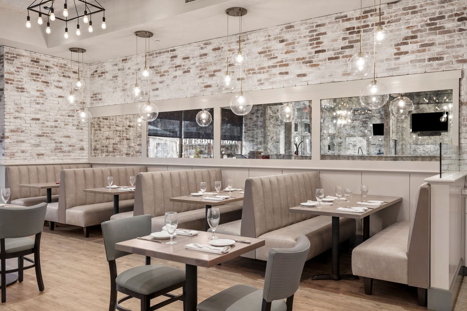 Elegant restaurant dining room with tufted booths, mirrored walls, and set tables under warm chandeliers