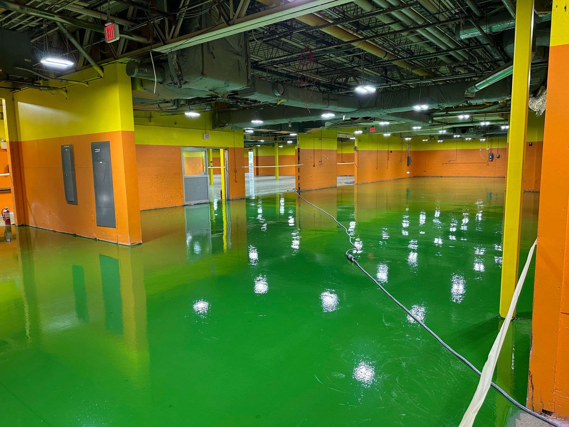 Empty indoor industrial space with glossy green floor, orange walls, and exposed ceiling beams