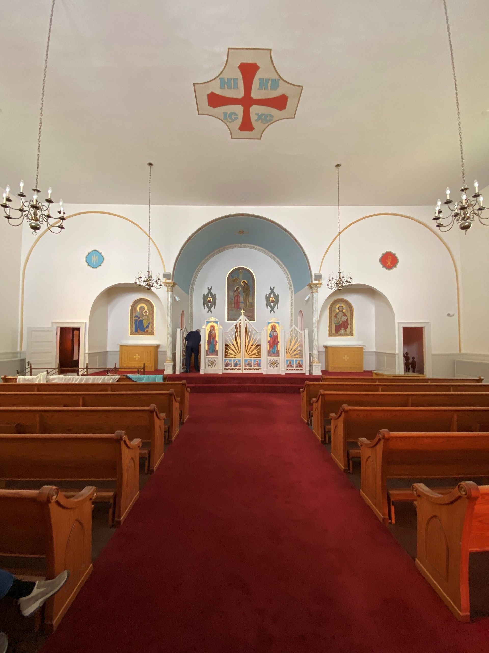 Church interior with red carpet, wooden pews, and an altar beneath arched white ceilings
