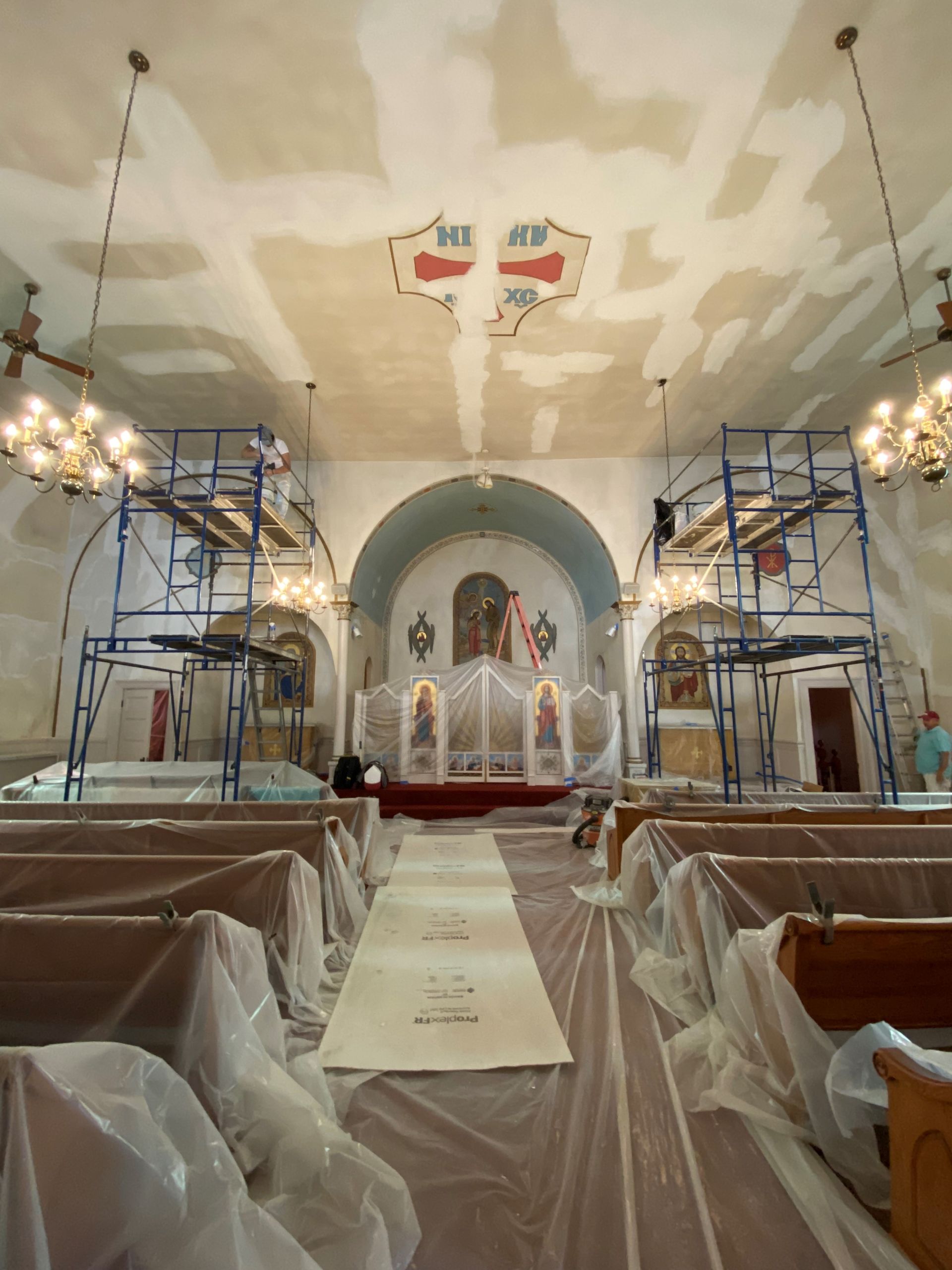 Church interior under renovation with scaffolding, draped pews, and a central aisle leading to the altar.