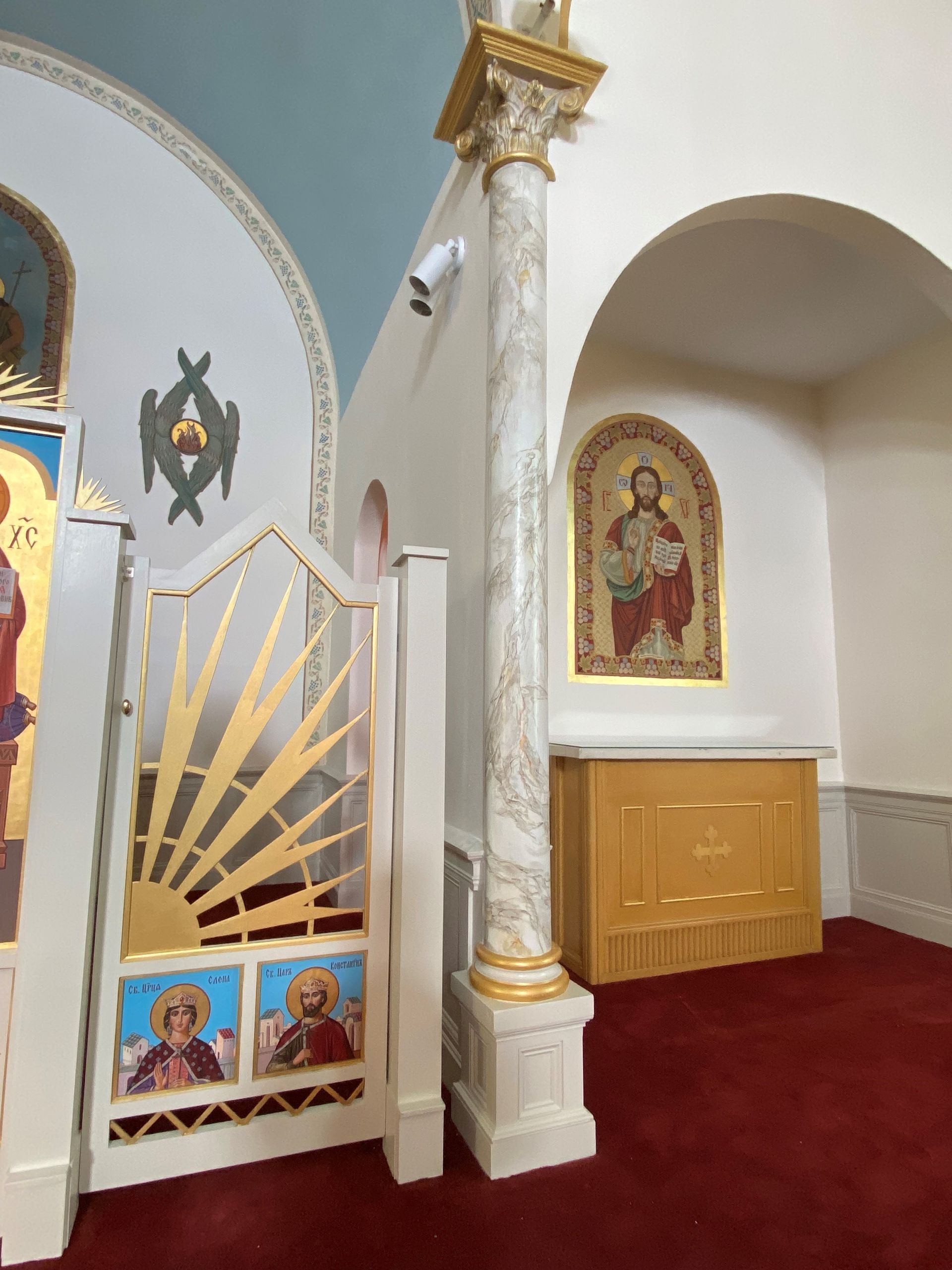 Ornate church interior with gold accents, religious icons, white archways, and red carpet.
