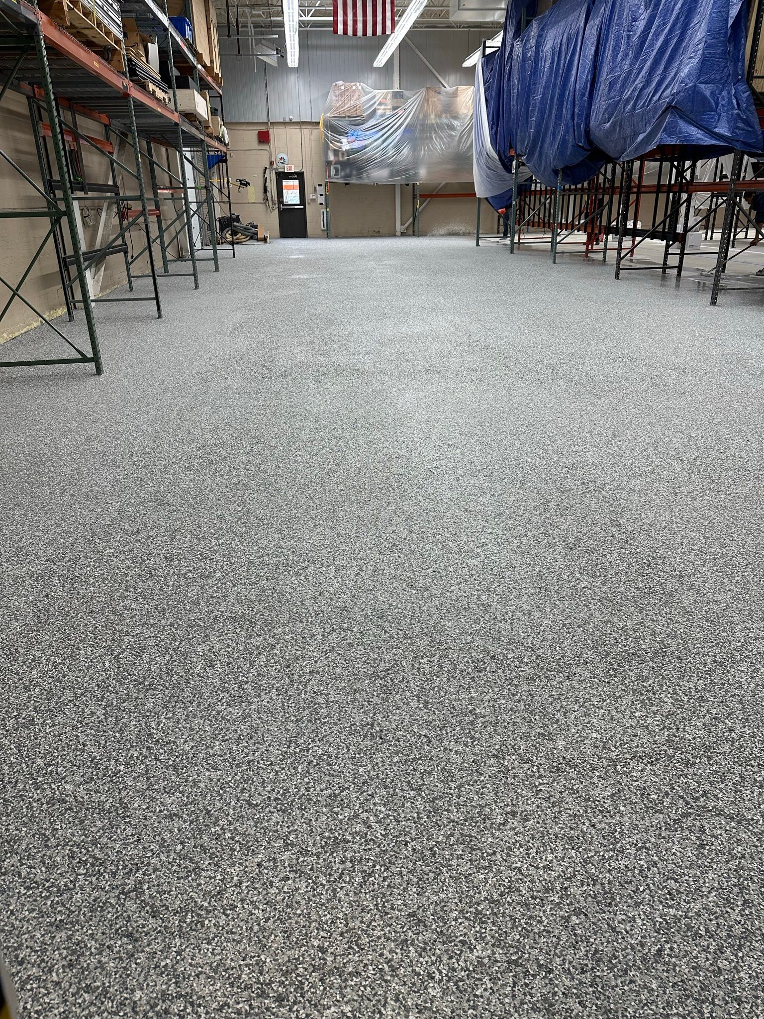 Speckled gray floor in a workshop or warehouse aisle with tables and equipment on both sides