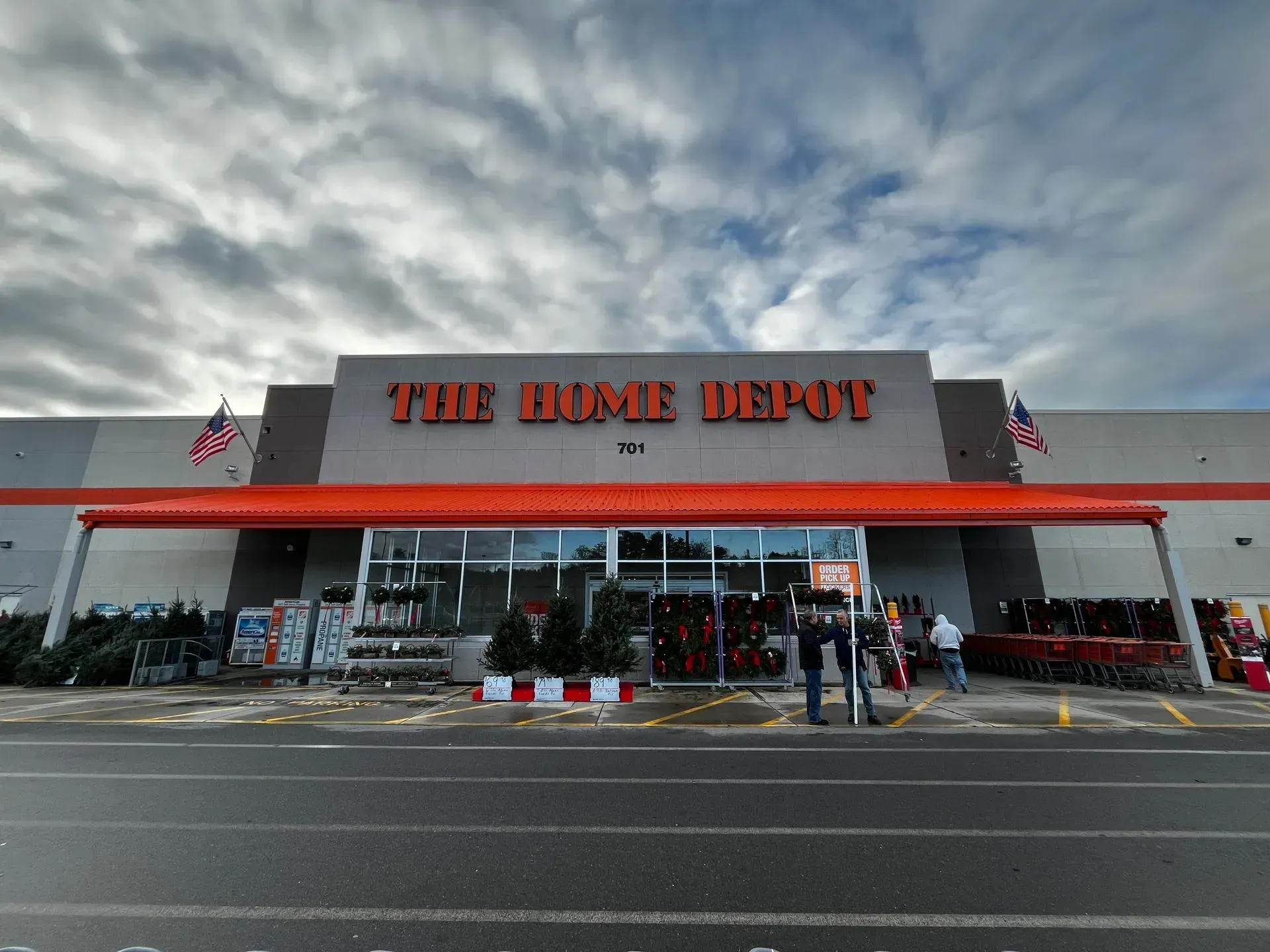 Home Depot storefront with orange sign and flags under a cloudy sky