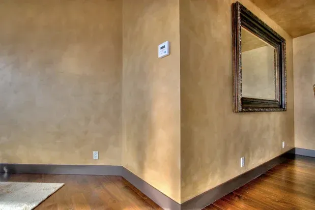 Empty beige hallway corner with wood floor, brown baseboards, and a wall mirror.