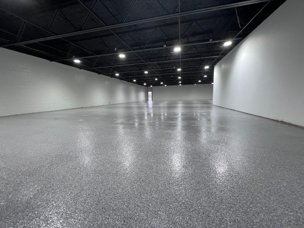 Empty indoor hall with gray floor, white walls, and black ceiling lights, viewed from one end