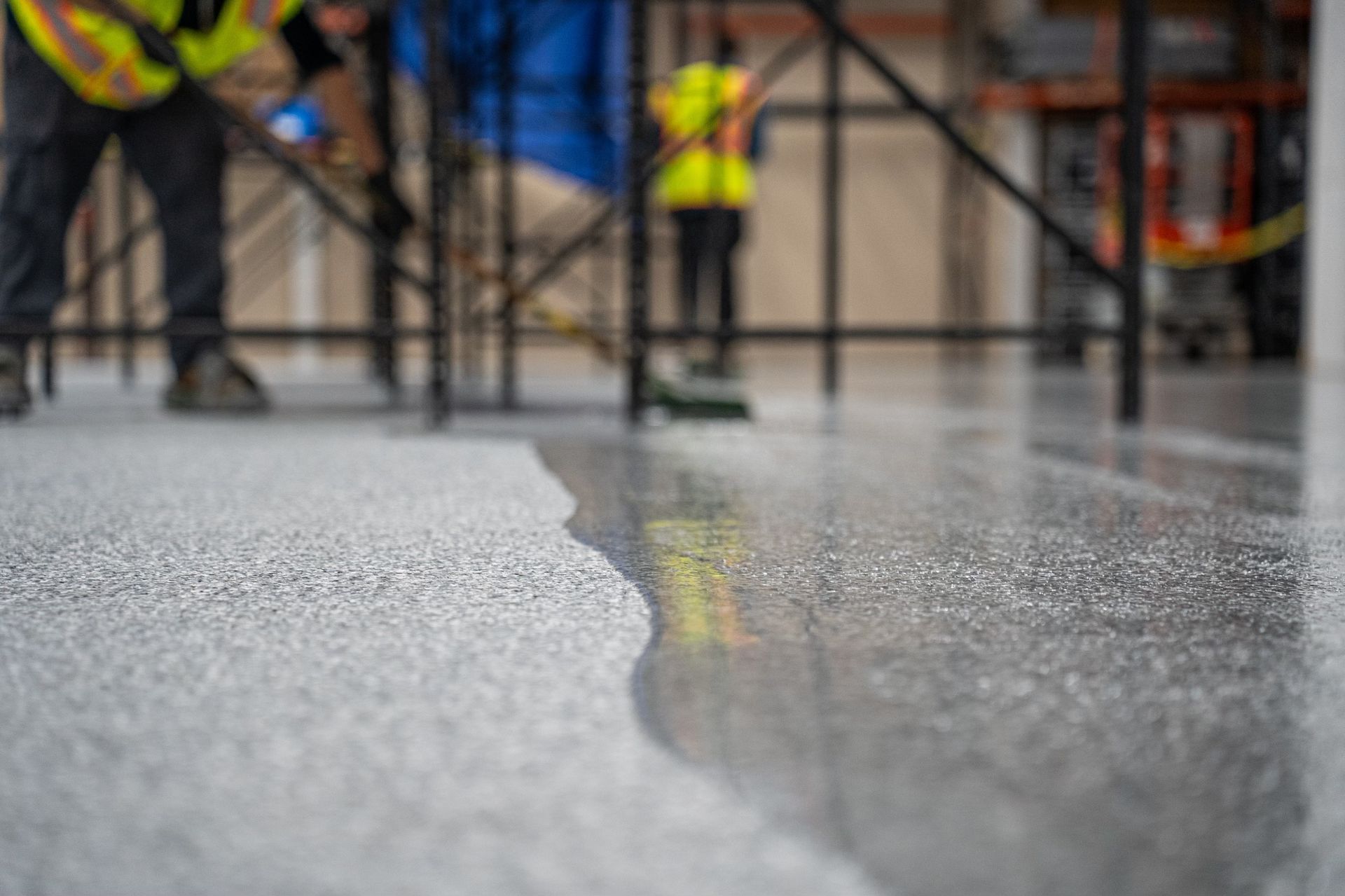 Rain-slick street with blurred workers in reflective vests near barricades and an orange traffic cone