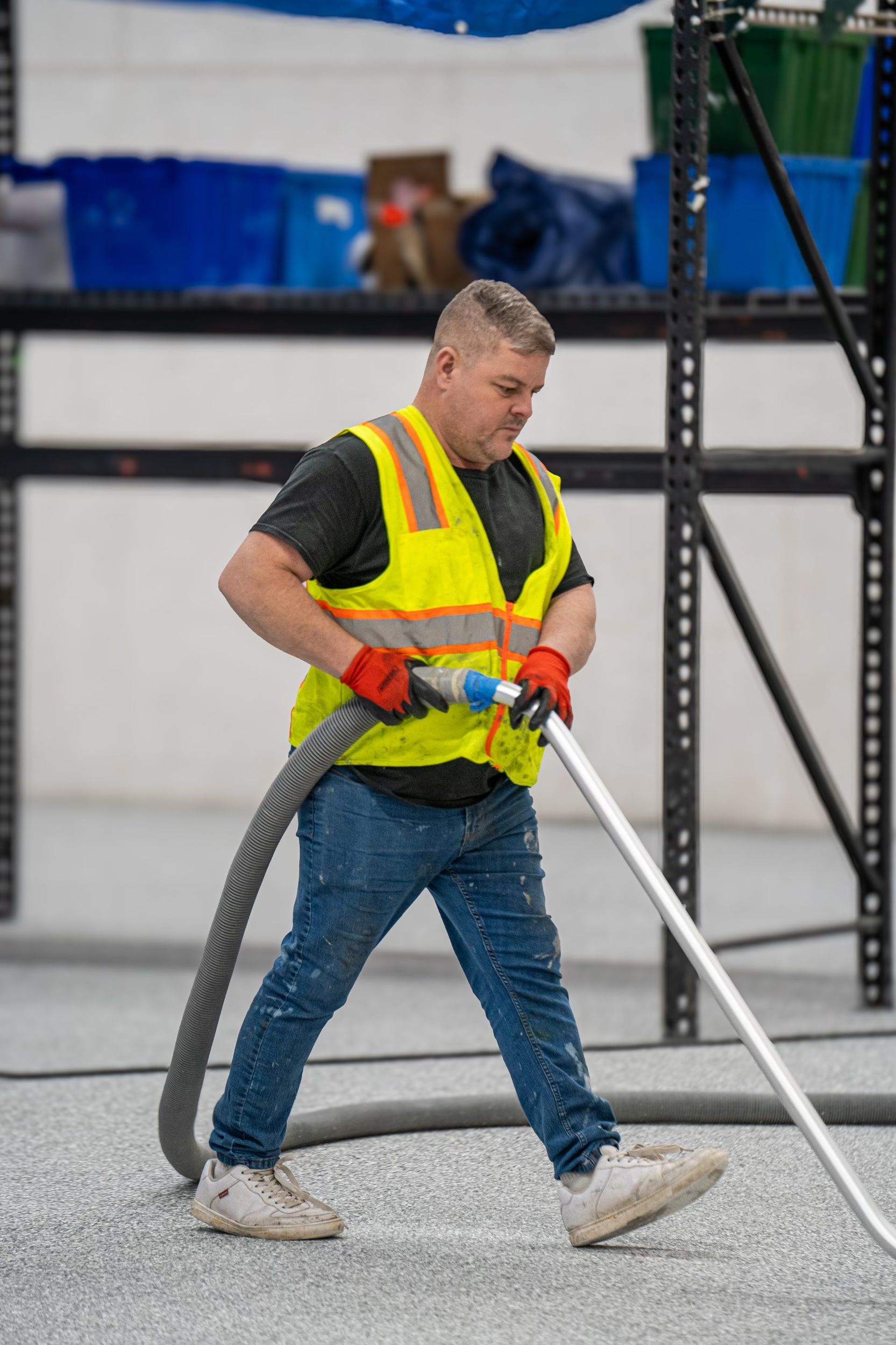 Worker in a yellow safety vest spraying material with a hose on a construction site