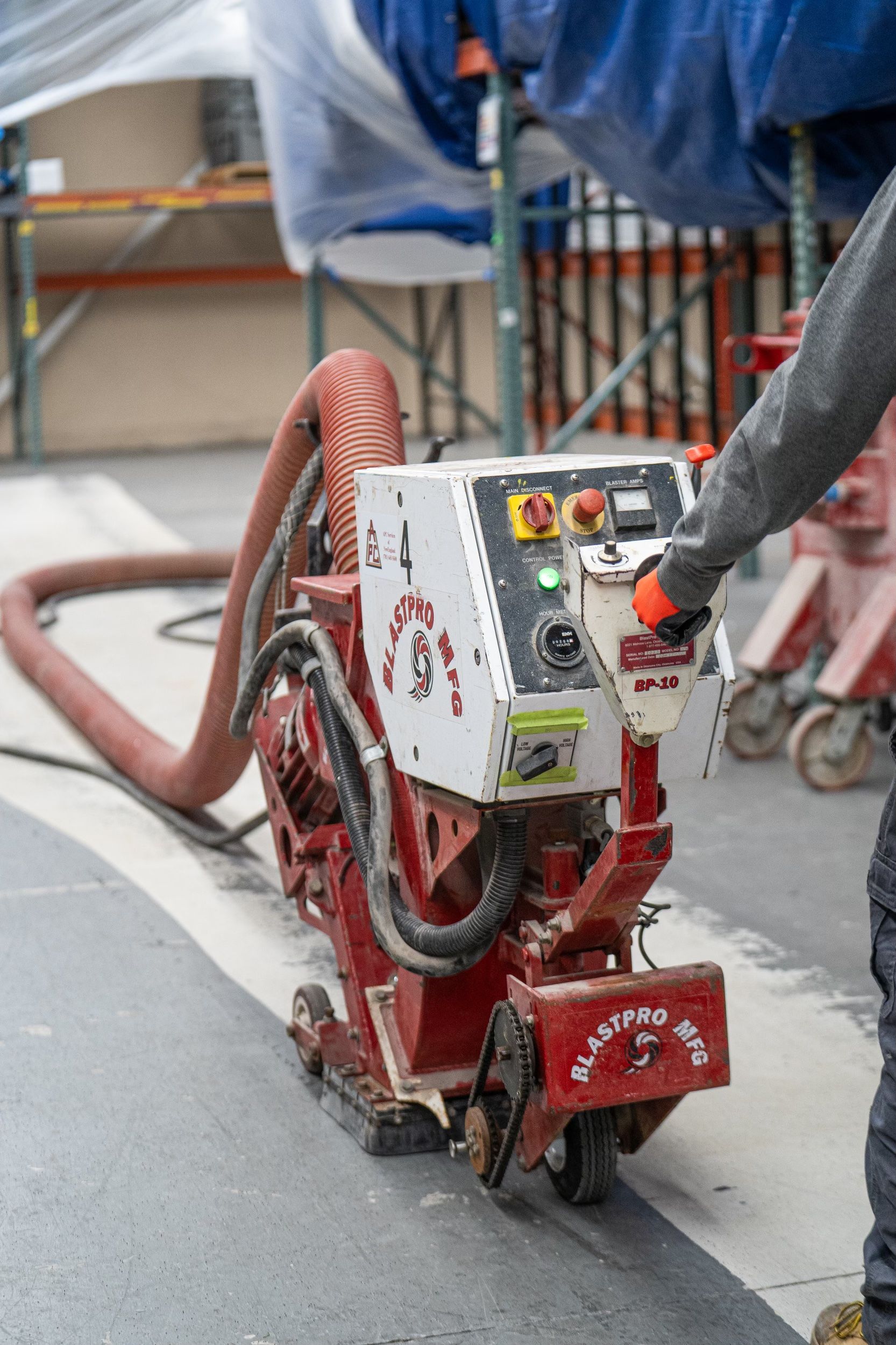 Worker operating a red floor grinding machine on a construction site floor