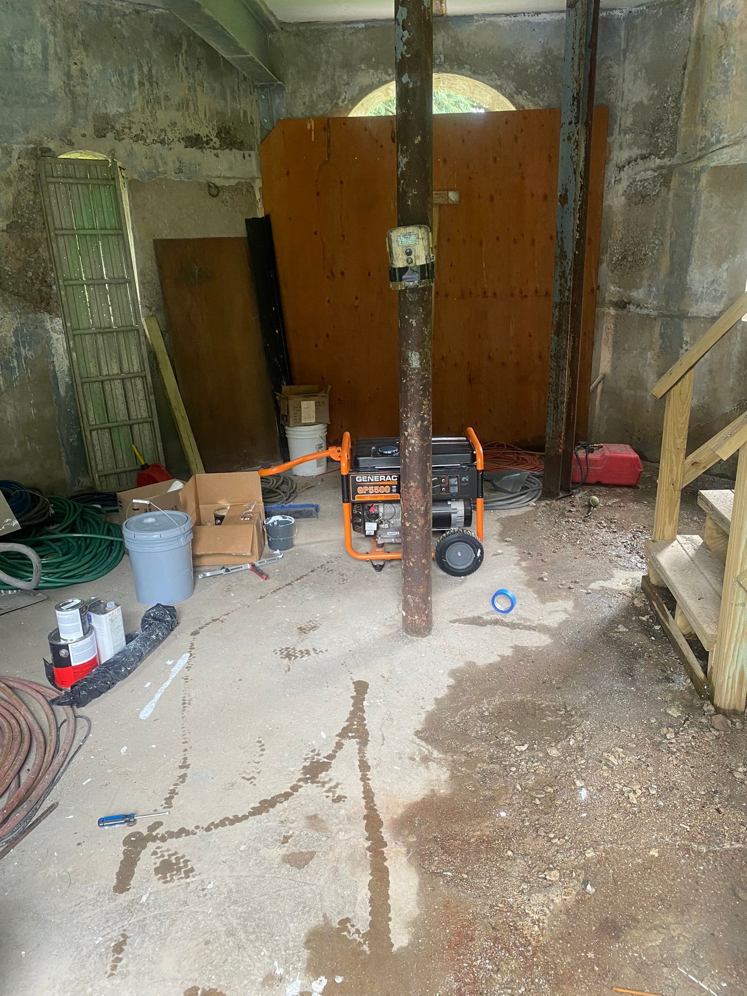 Cluttered shed with tools, cabinets, and a central pole on a concrete floor.