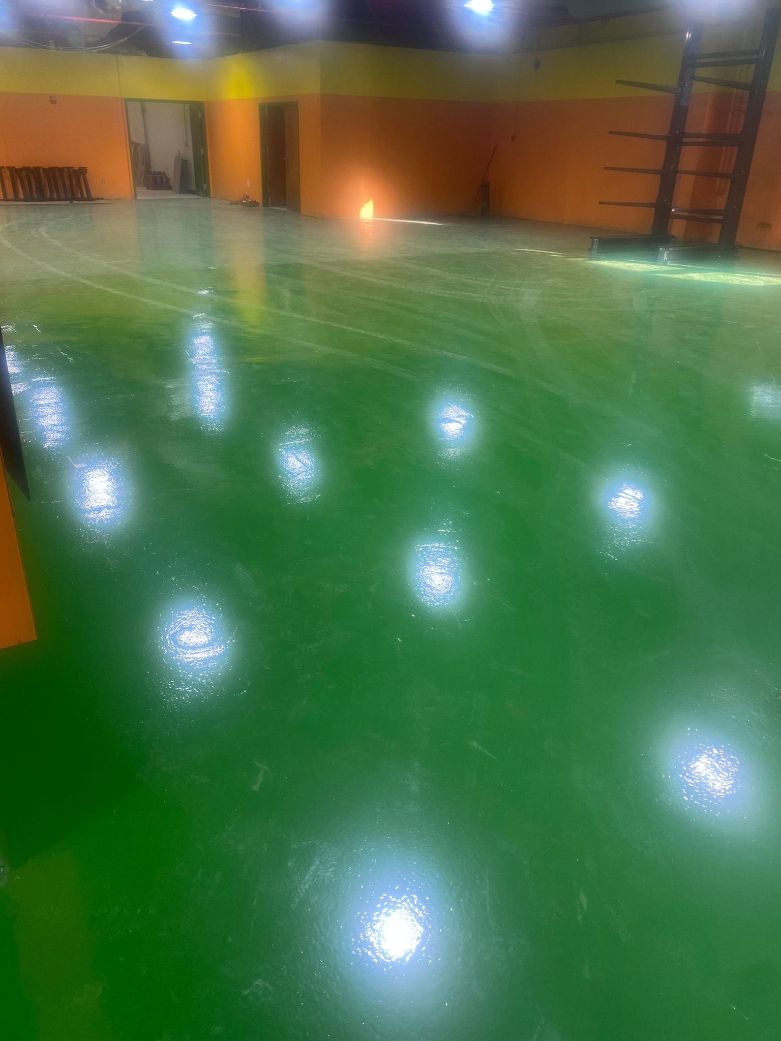 Empty indoor room with a glossy green floor, warm orange walls, and bright lights reflecting on the surface