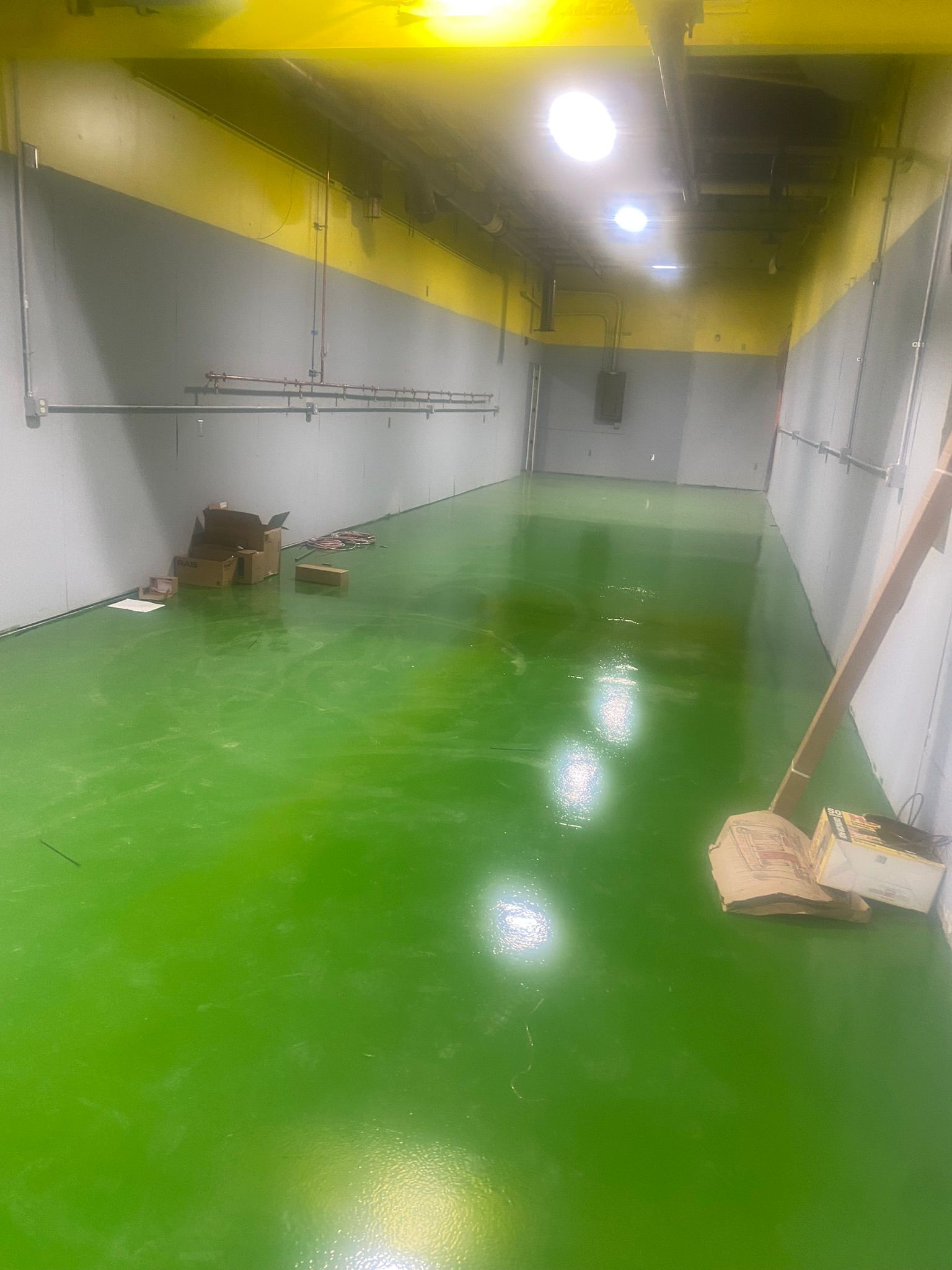 Empty industrial room with glossy green floor, white walls, yellow ceiling, and a broom leaning on the right.