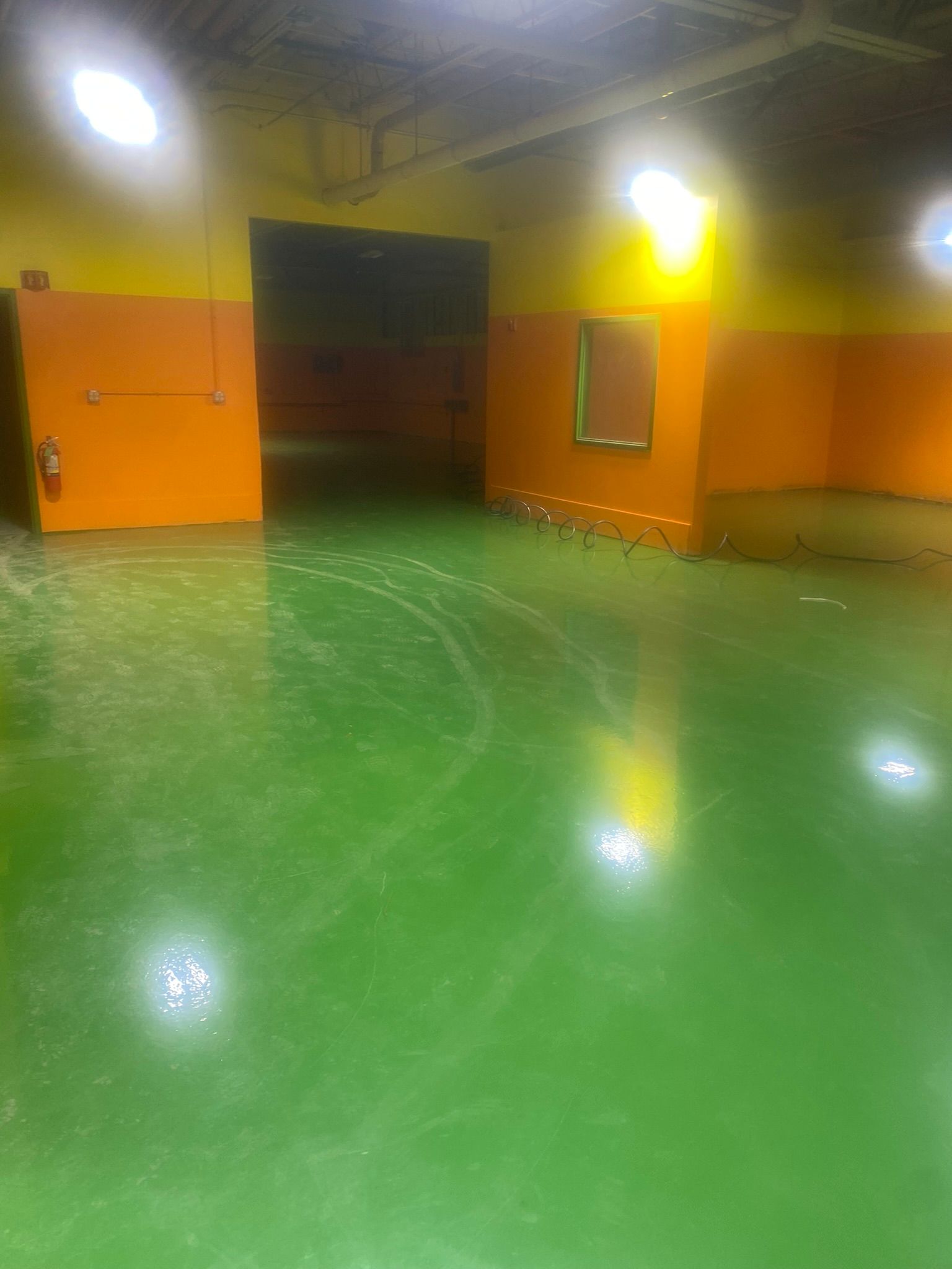 Empty indoor room with glossy green floor, orange walls, bright lights, and an open doorway.