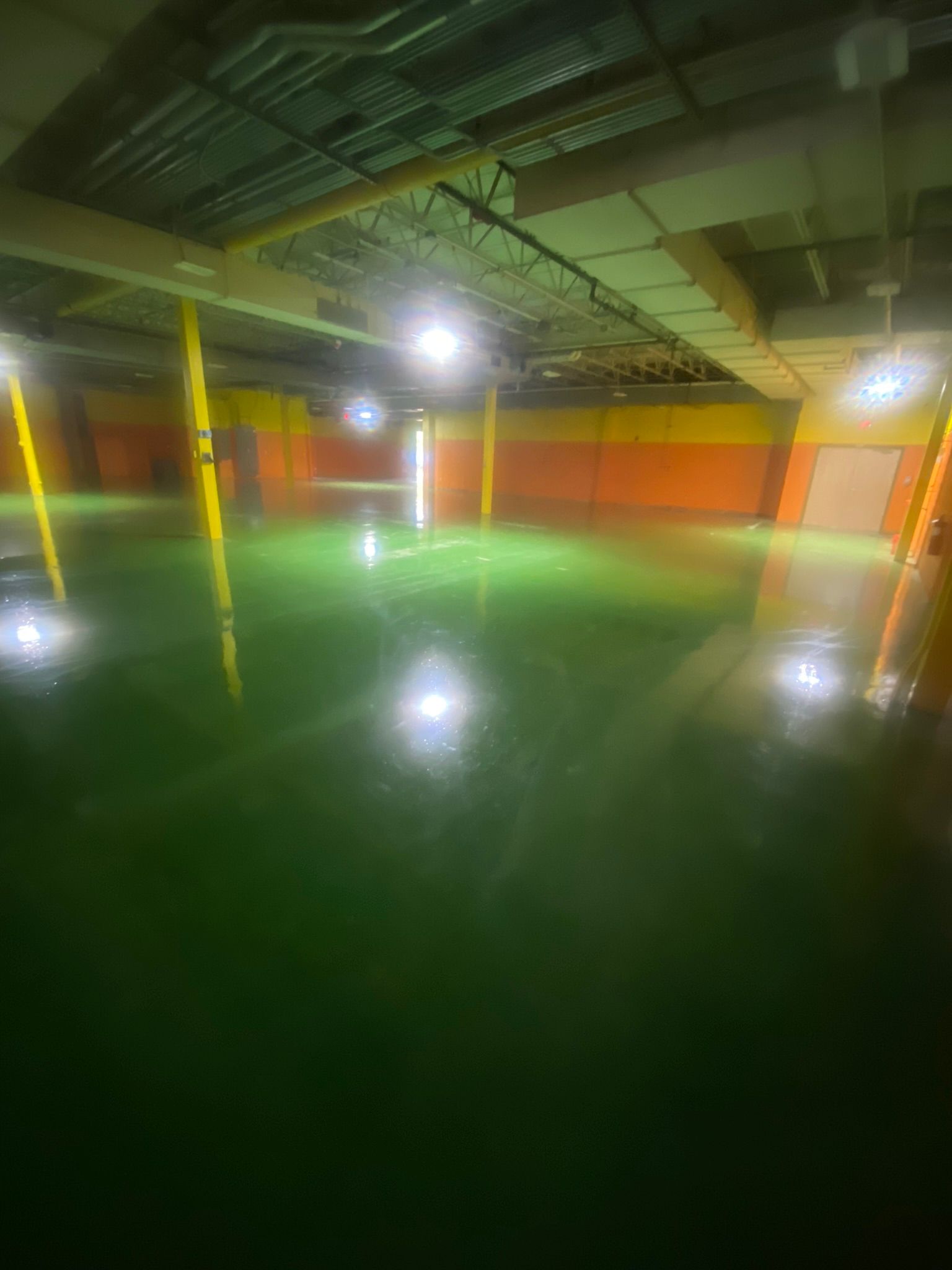 Empty indoor parking garage with green floor, yellow pillars, and bright overhead lights.