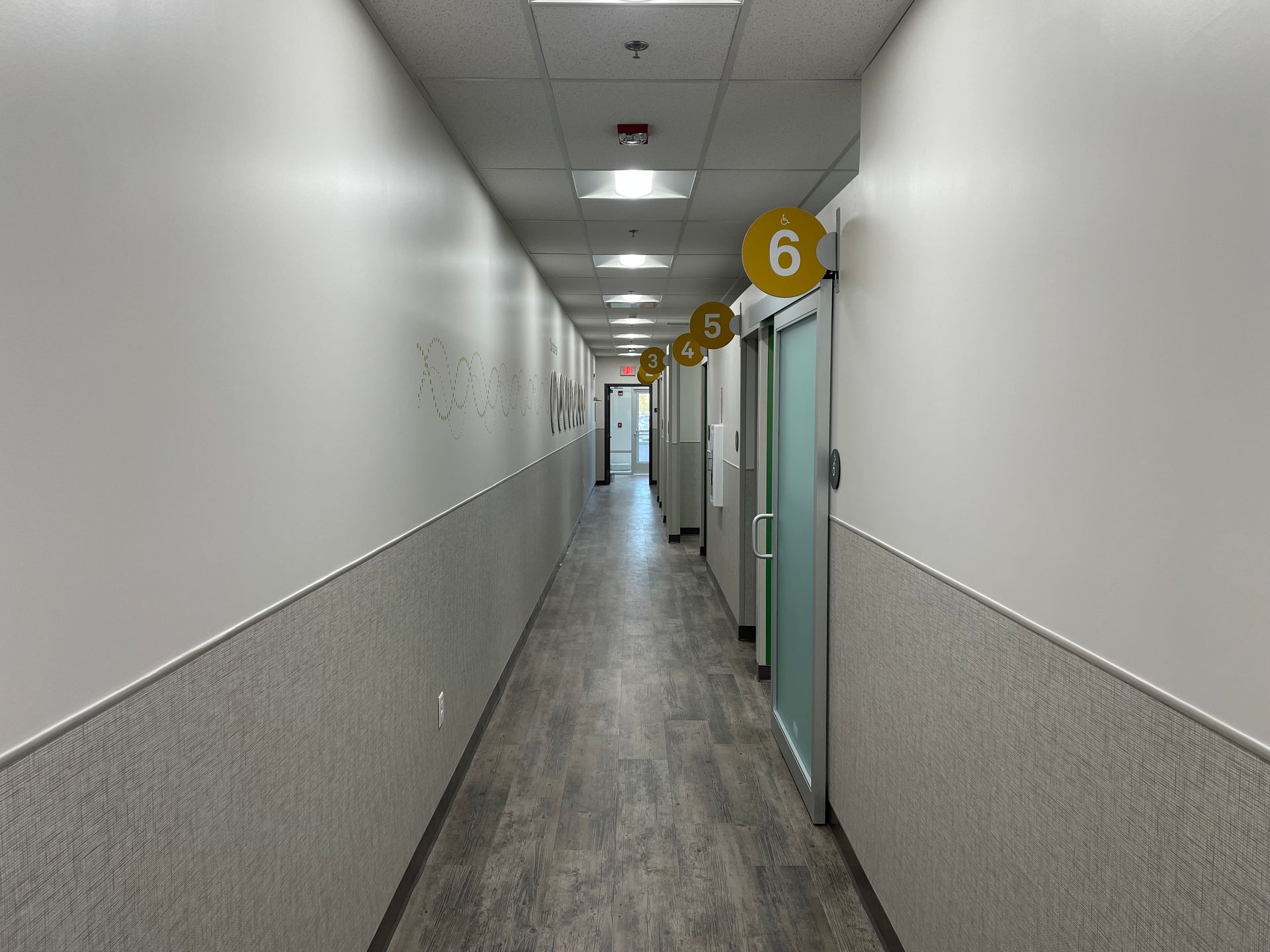 Long narrow hallway with white walls, gray floor, and numbered room doors on the right