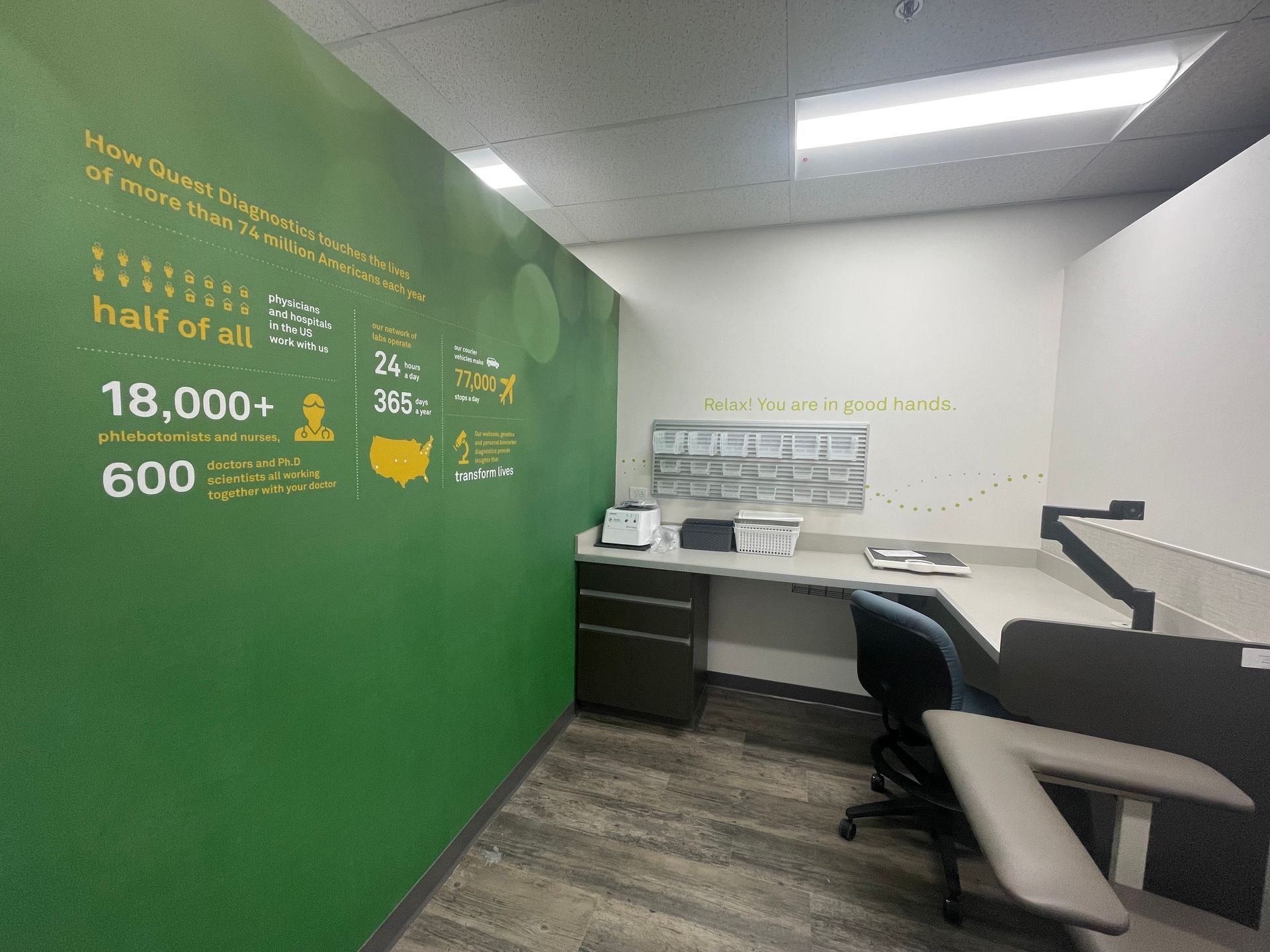 Small office workspace with green accent wall, white desk, black chair, and fluorescent ceiling lights