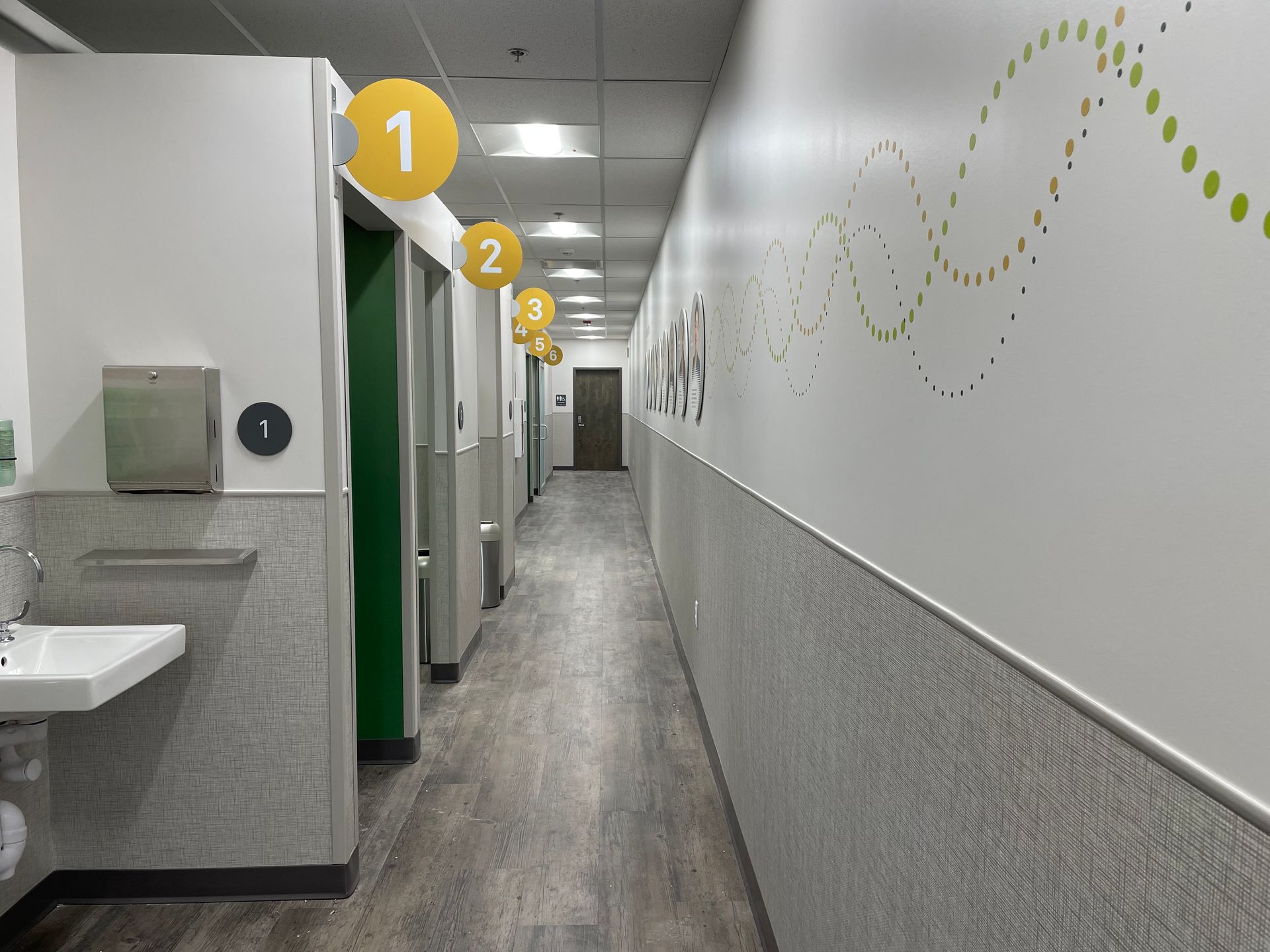 Public restroom hallway with sinks, stalls, and numbered accessibility signs on the wall.