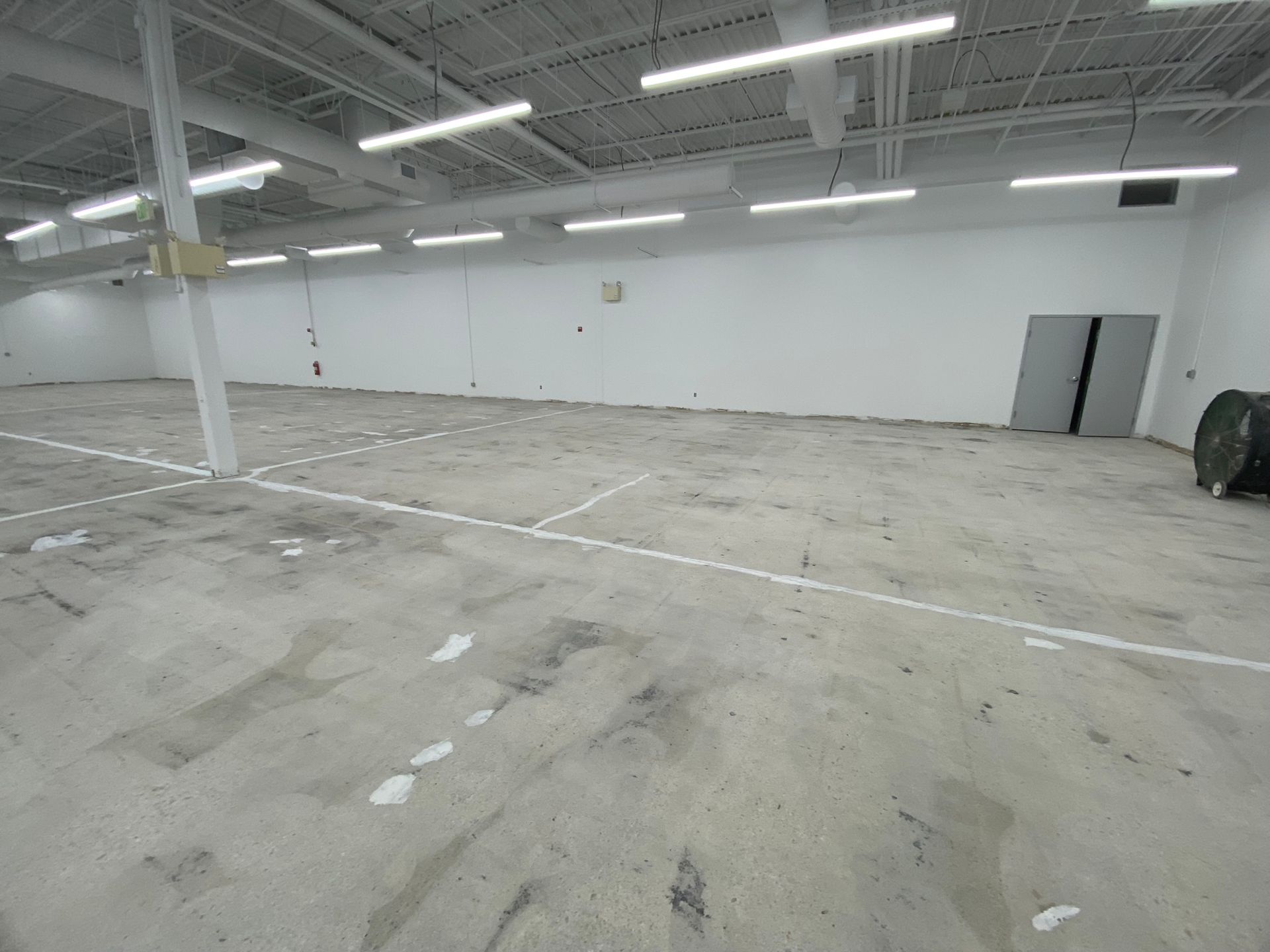 Empty industrial warehouse with white walls, concrete floor, and overhead fluorescent lights
