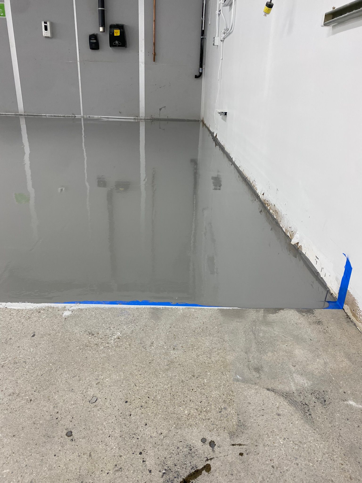 Flooded indoor room with standing gray water beside a dry concrete floor and unfinished walls
