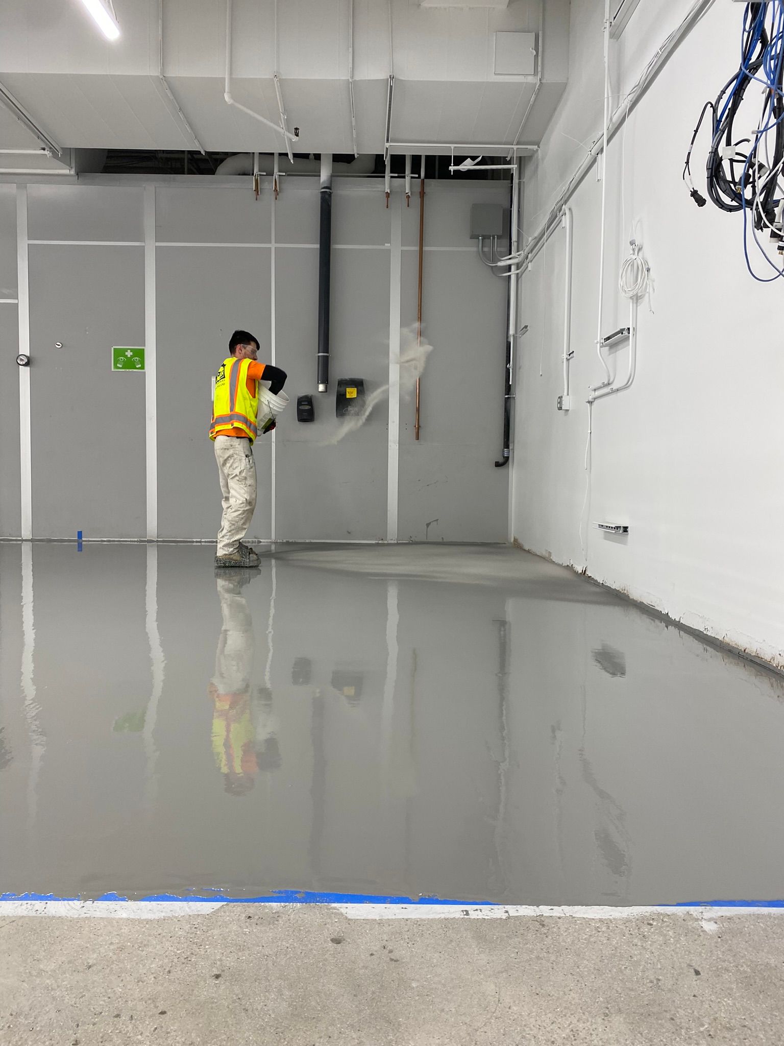 Worker in a yellow safety vest inspecting a glossy concrete floor in a large industrial room