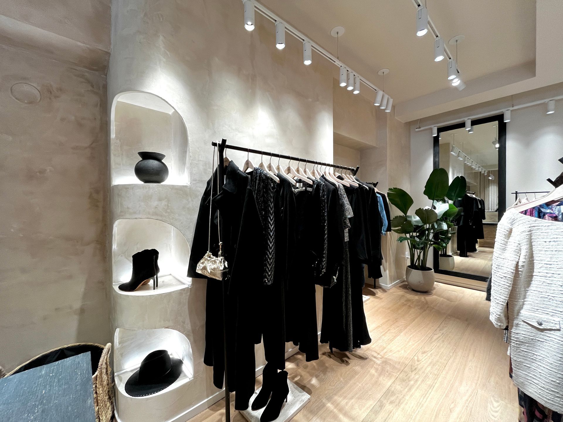 Modern boutique interior with black clothing racks, white shelves, and warm wood flooring
