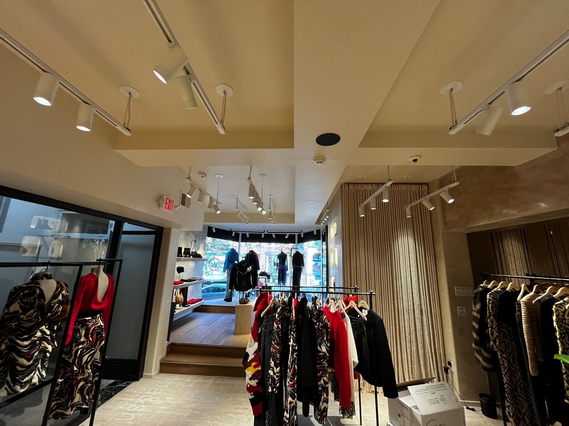 Clothing boutique interior with racks of colorful garments and a seating area near the front window.