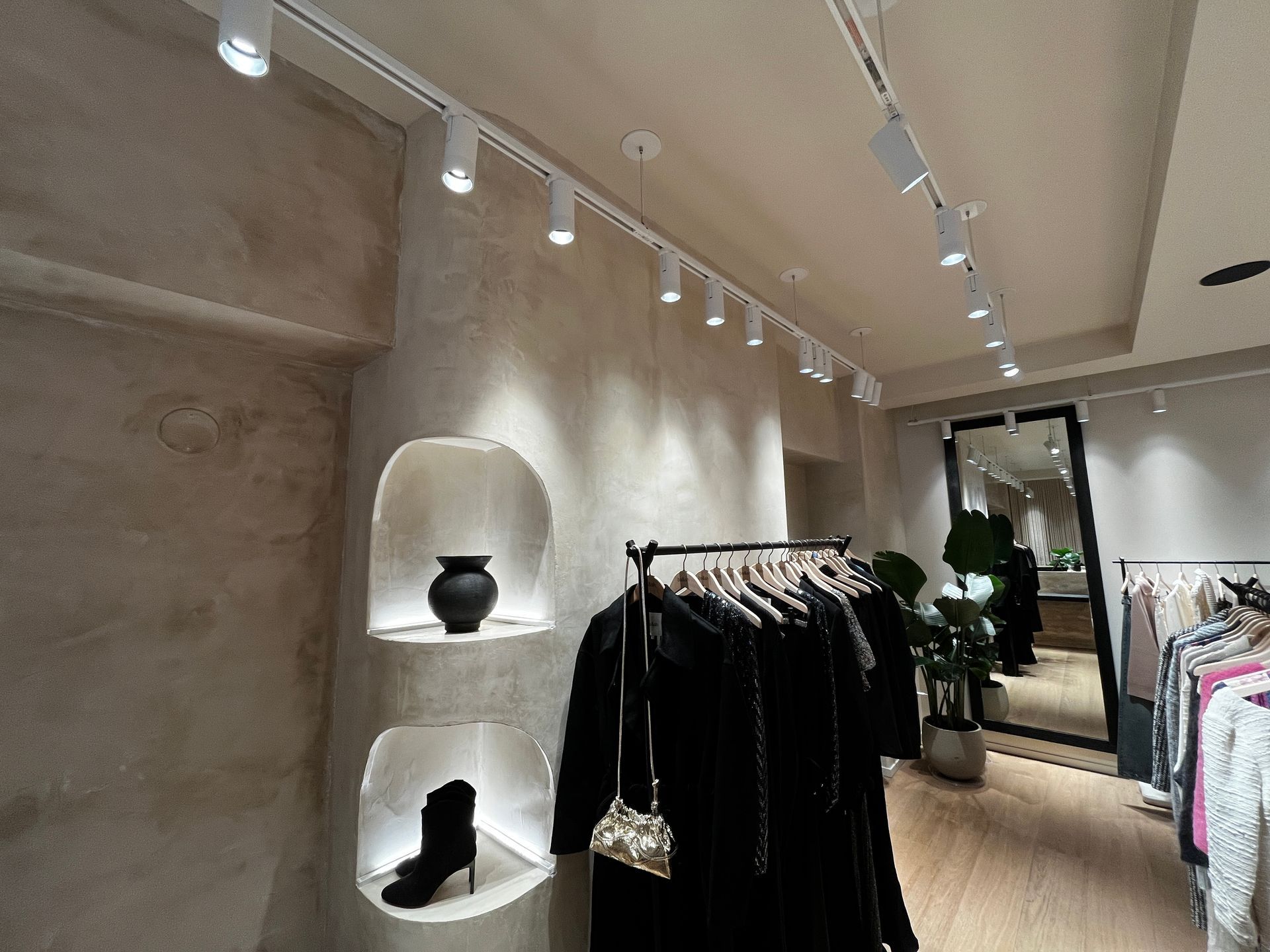 Minimalist clothing boutique with racks of black garments, shelves, and track lighting along a textured wall