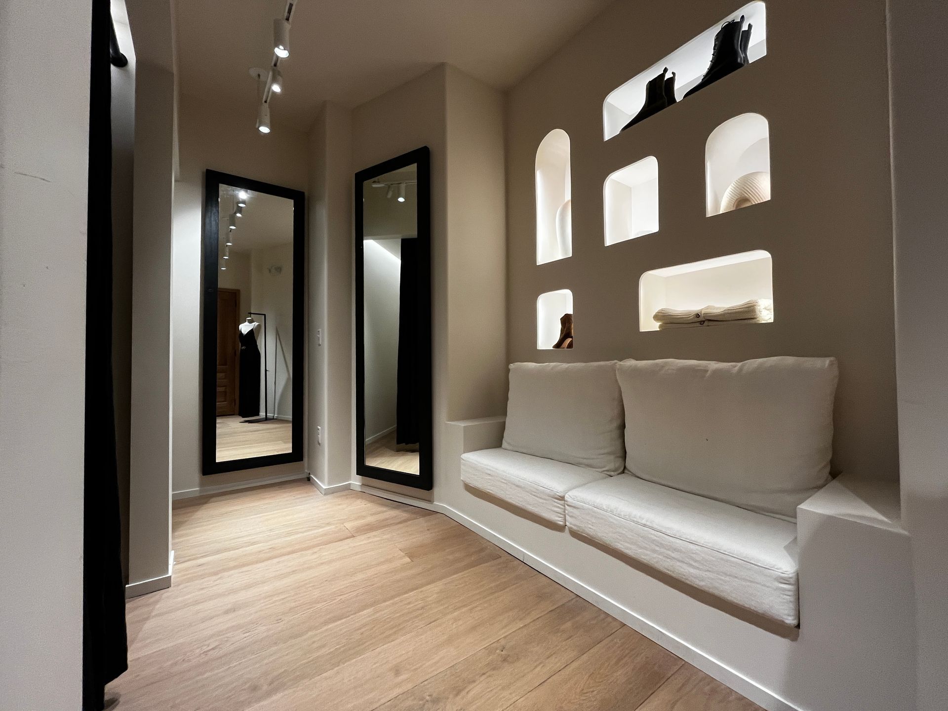 Modern minimalist hallway with wood floor, recessed wall niches, and a built-in white bench with cushions