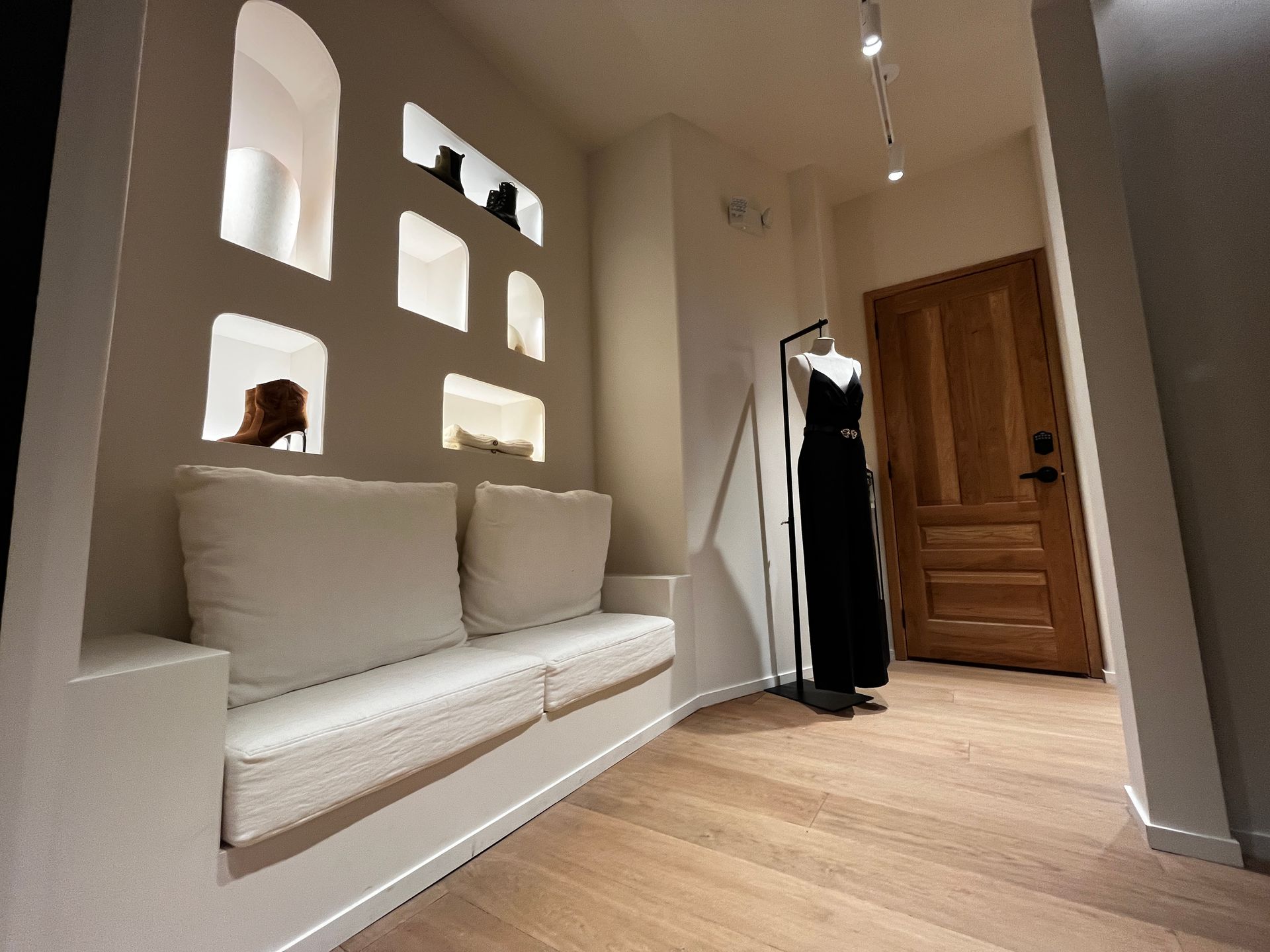 Modern entryway with built-in bench, arched wall niches, wood door, and hanging coat.