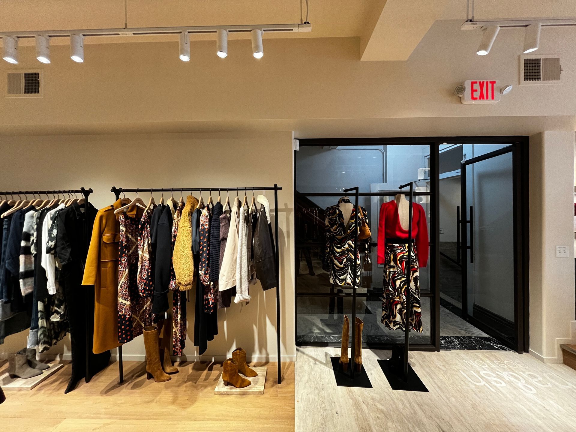 Clothing racks in a retail store near a glass entrance with an EXIT sign.