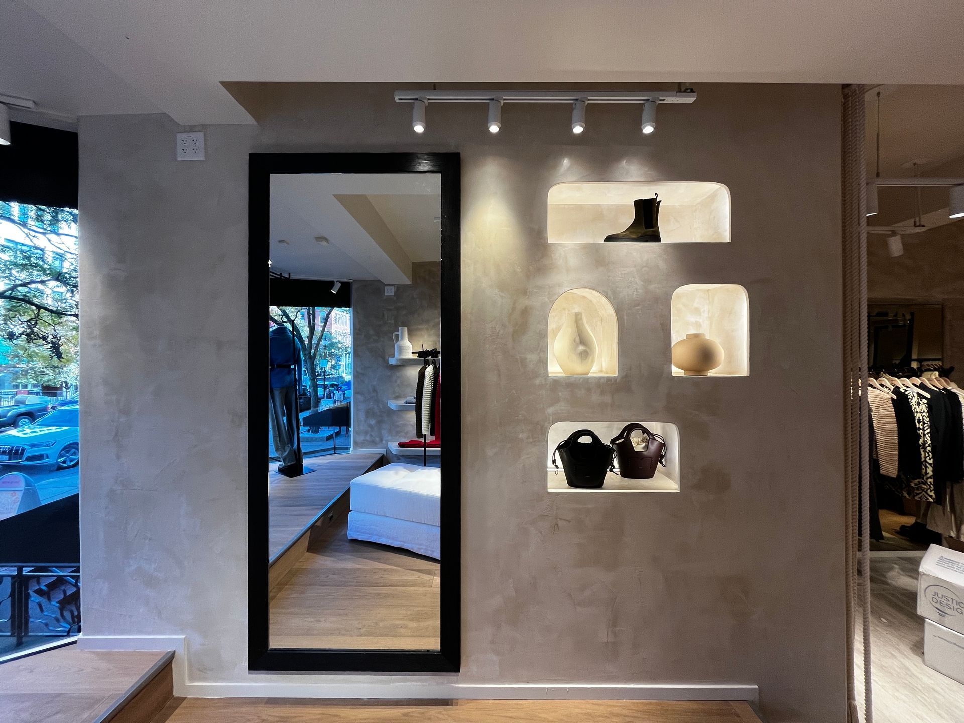 Modern clothing boutique with a full-length mirror, lit display shelves, and racks of clothes