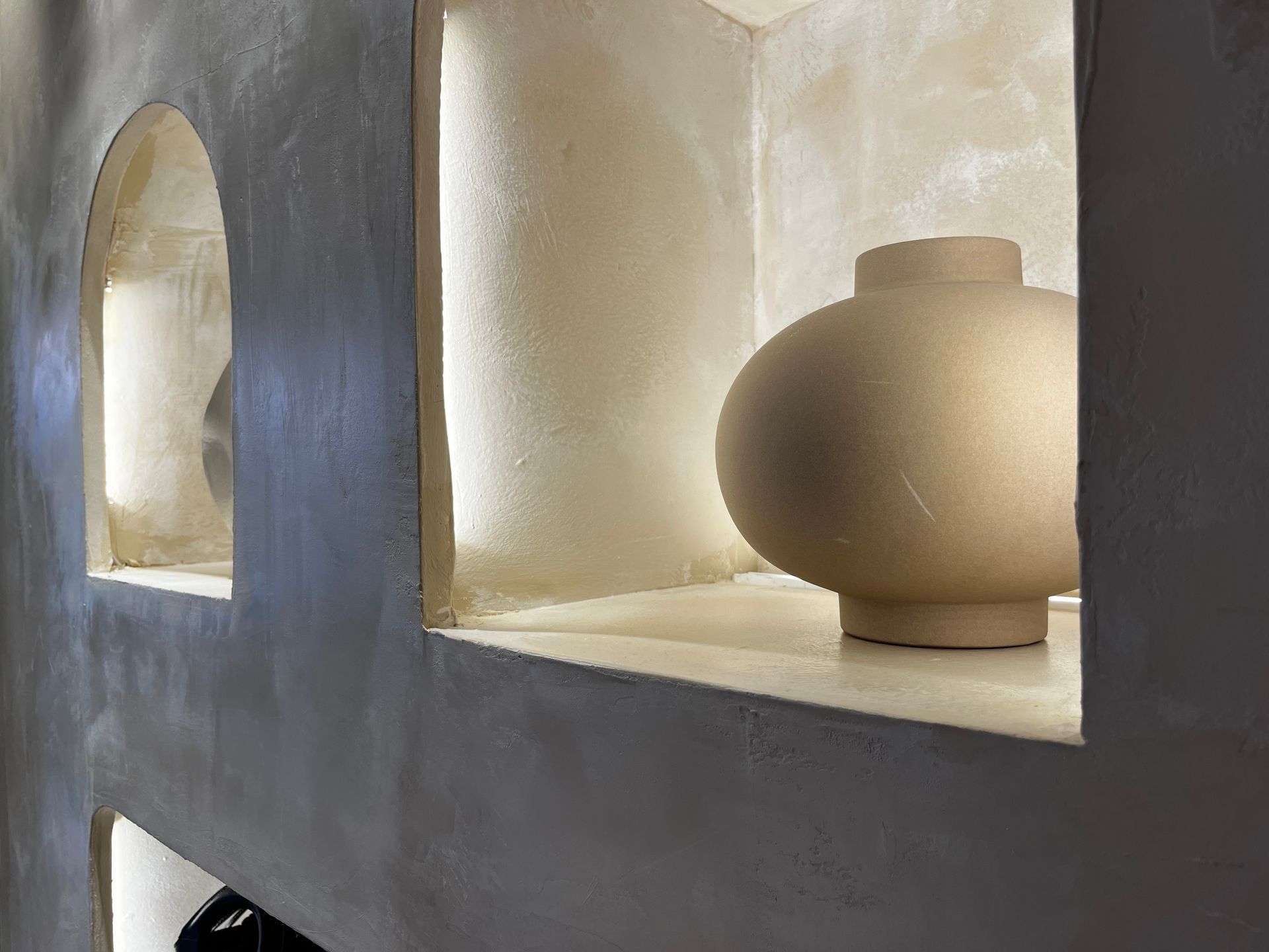 Minimalist shelf with white ceramic vases and arched cutouts, lit by soft natural light