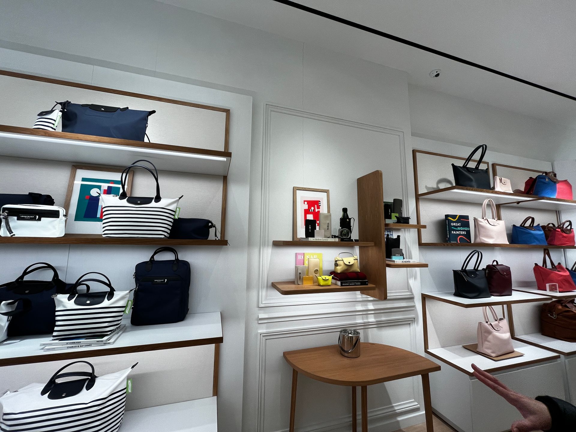 Shelves of handbags and accessories in a bright boutique with a small round table and stool