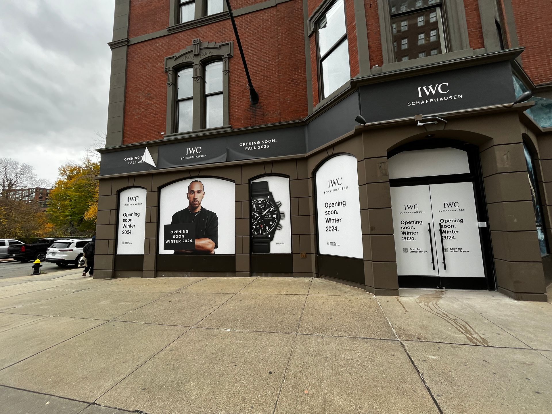 Storefront with large window ads and black awnings on a city street corner under cloudy skies